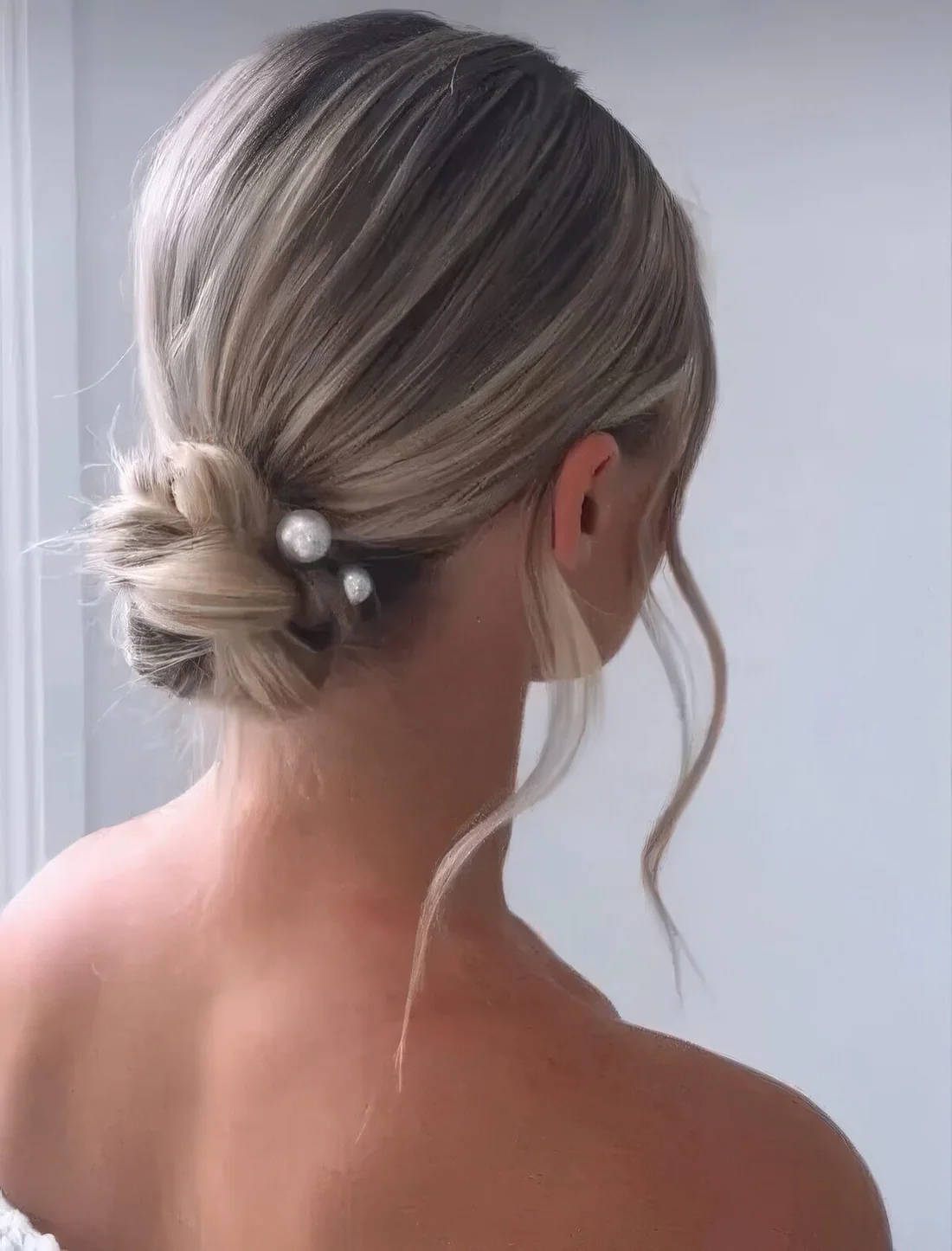 Woven twisted low bun with pearl hair pins and waves down.