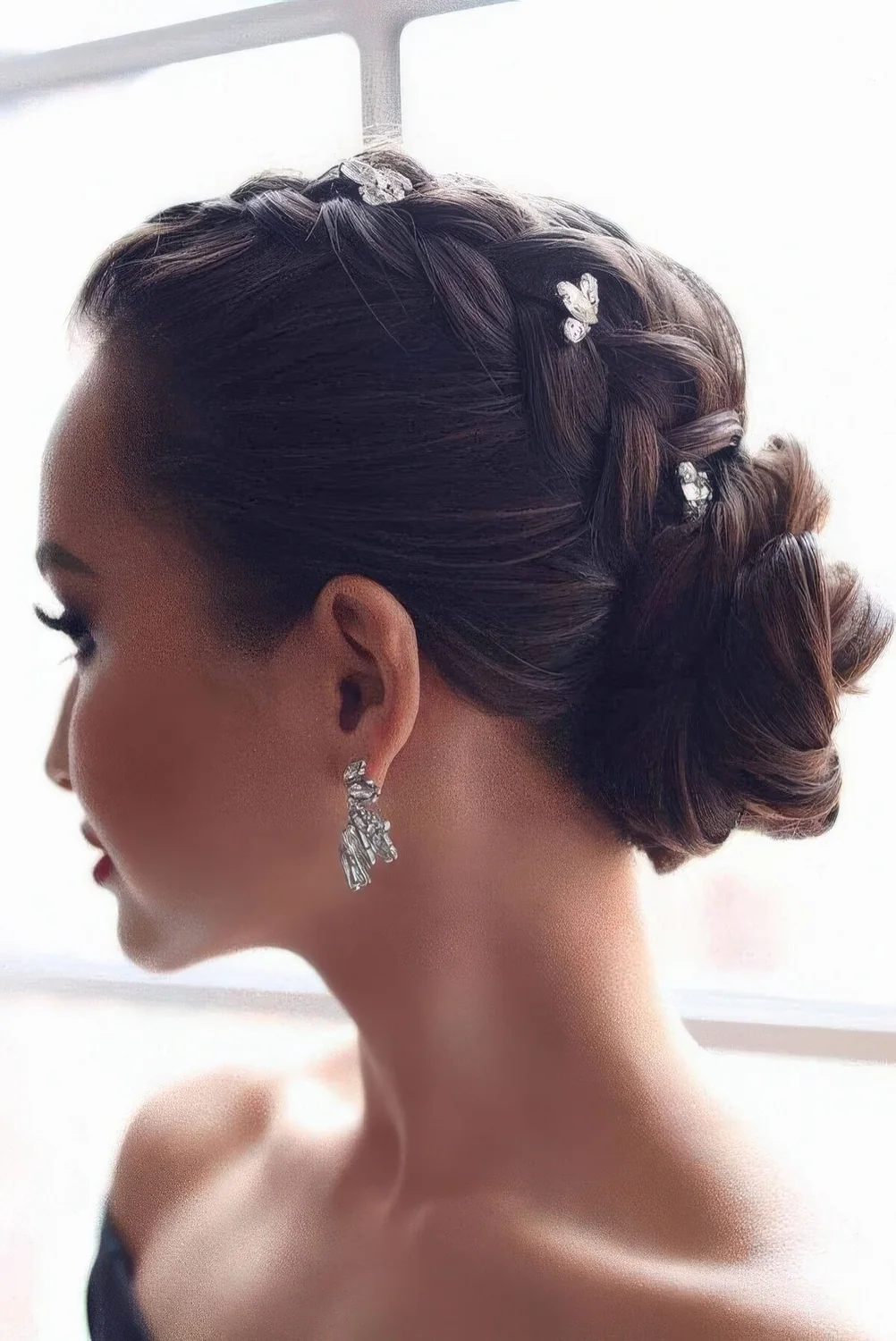 Glam updo with a braid on top and a low bun accented with rhinestone hairpins.