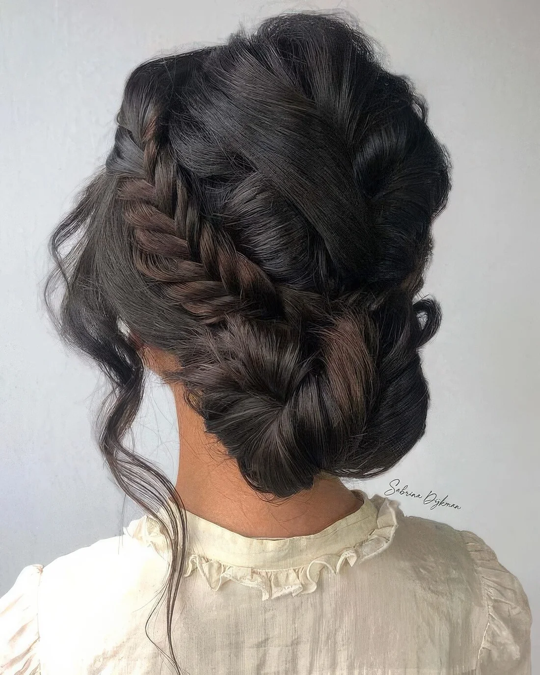 Low twisted updo with a side fishtail braid and face-framing hair.