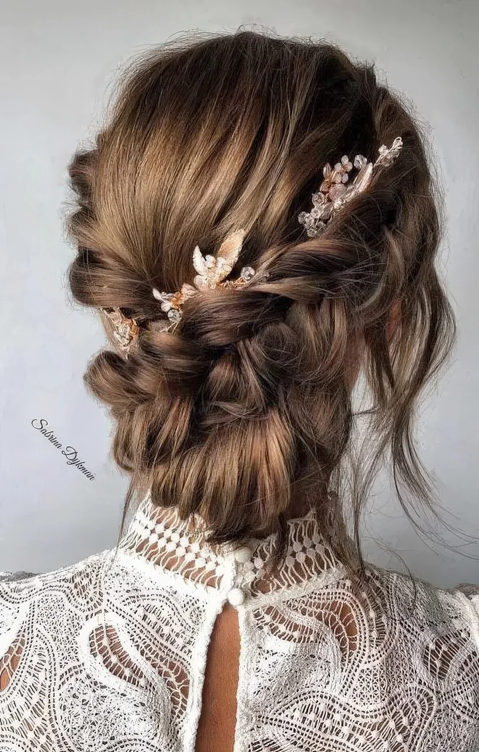 Braided low updo with two side braids, a bump, a low bun and face-framing locks plus some beaded hair pieces.
