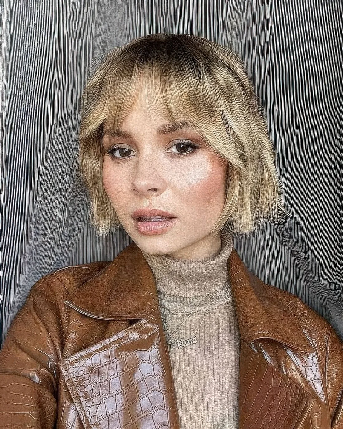 Relaxed blonde wavy jaw-length bob with wispy bangs.