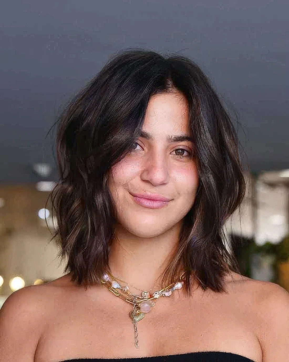 Dark brown layered lob on thick hair, with center part and highlights that give texture to the look.