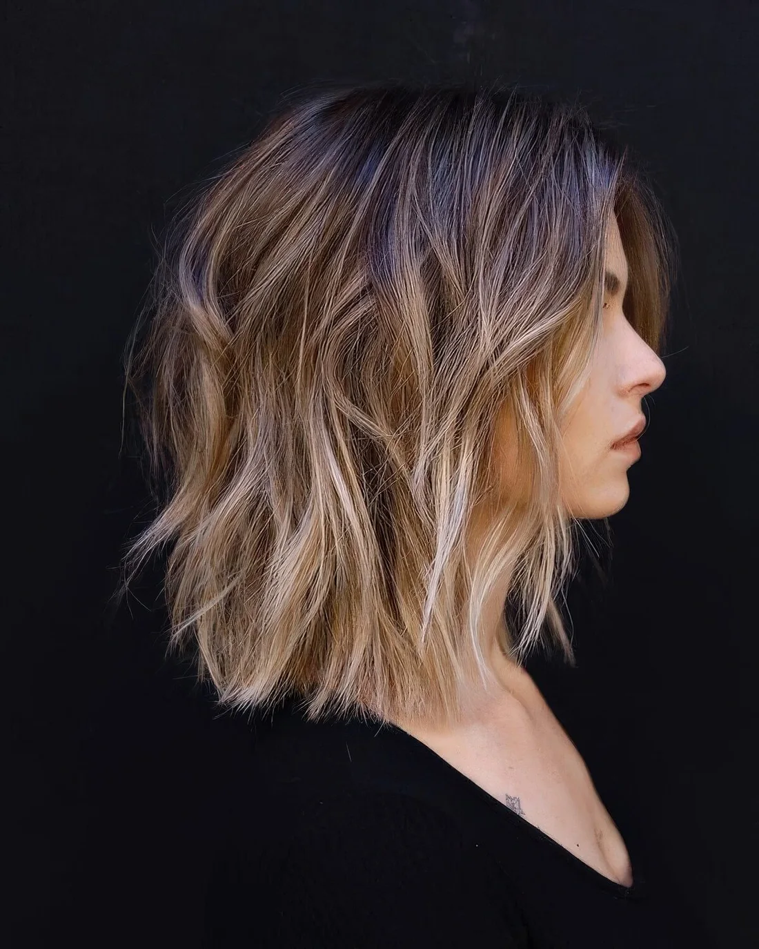 Layered long bob with a darker root and blonde highlights, with textured waves.