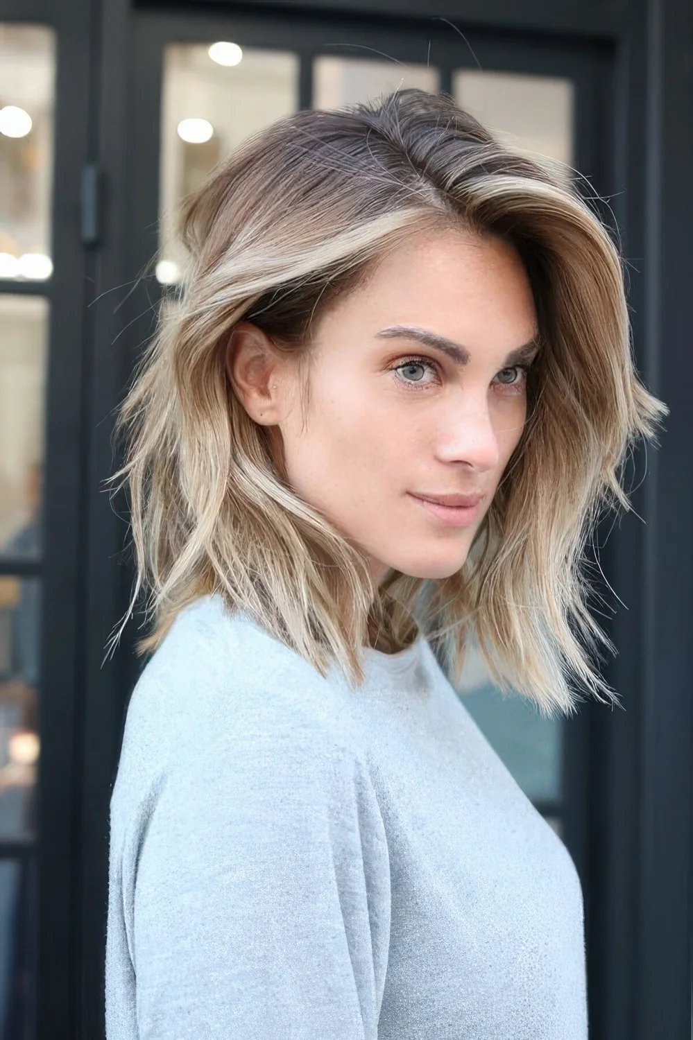 Layered long bob with blonde balayage and a darker root, with plenty of volume and texture.
