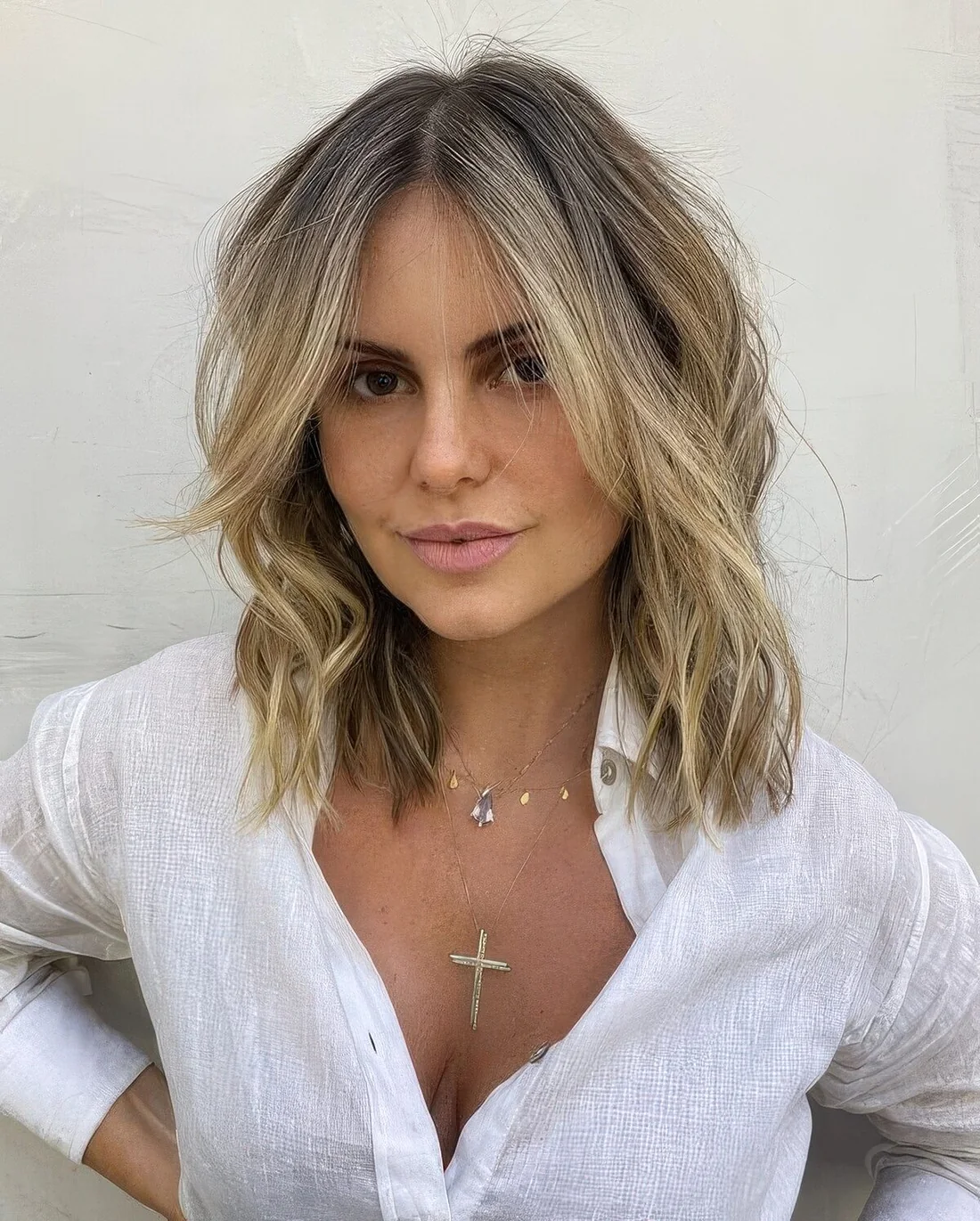 Long layered bob with blonde balayage, a darker root, face-framing bangs and waves and texture.