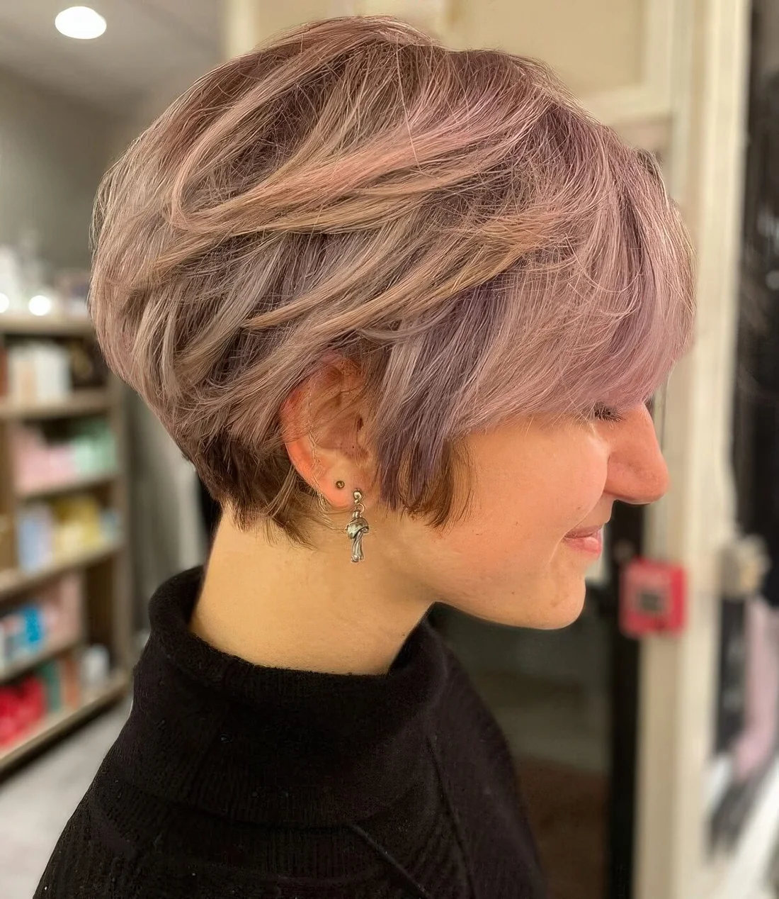 Layered pink pixie bob with longer sides and side bangs.