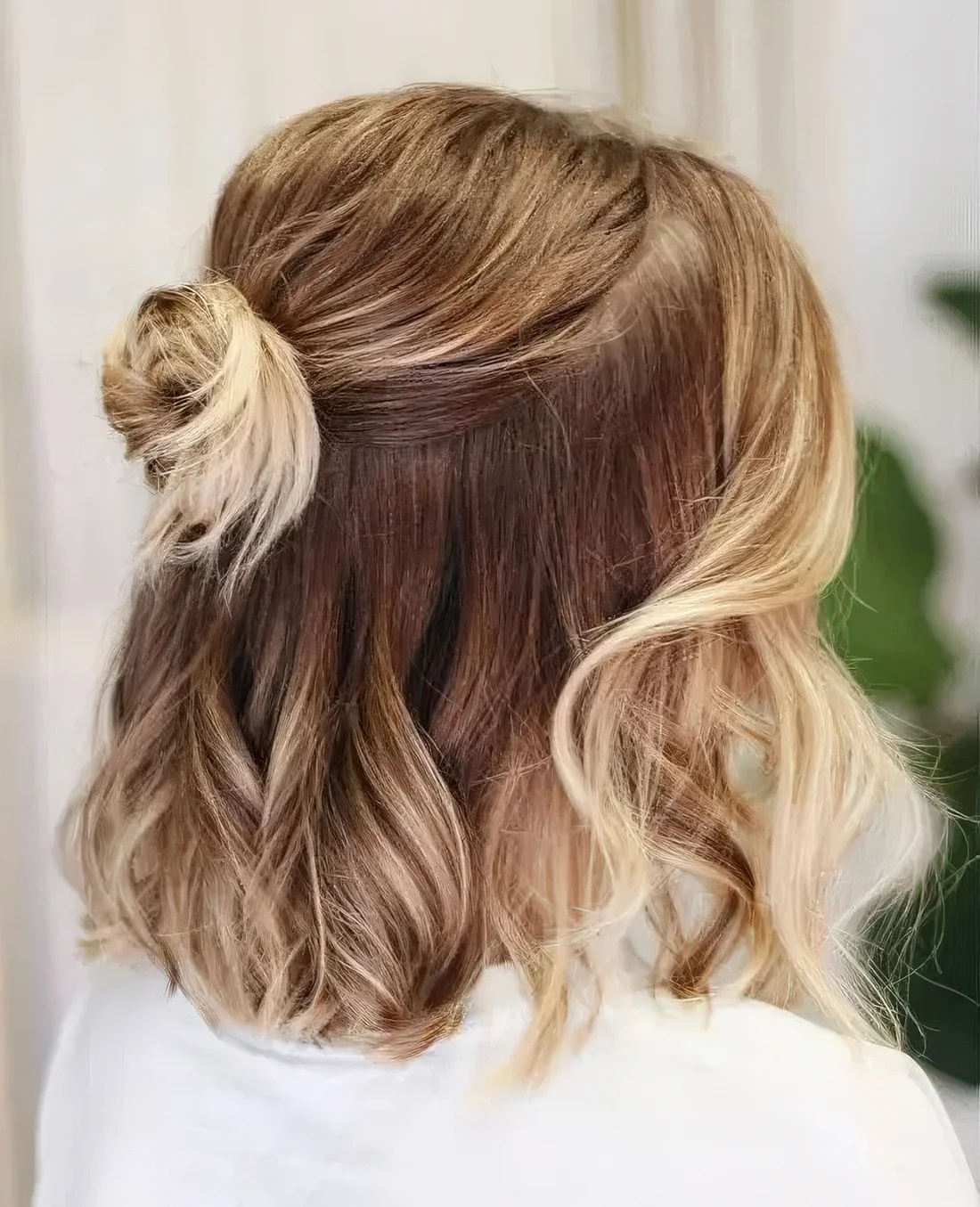 Medium hair half updo with a bump on top, a small bun and waves down plus face-framing hair.