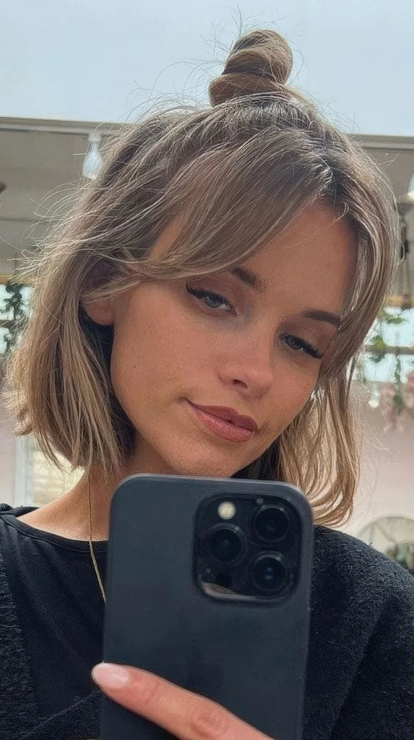 Half updo with a messy top knot, face-framing bangs and some bump.
