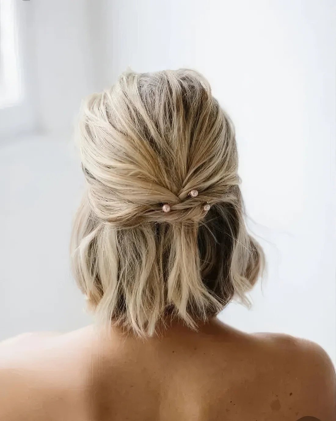 Short textural and wavy hair done into a half updo with blush pearl hairpins.