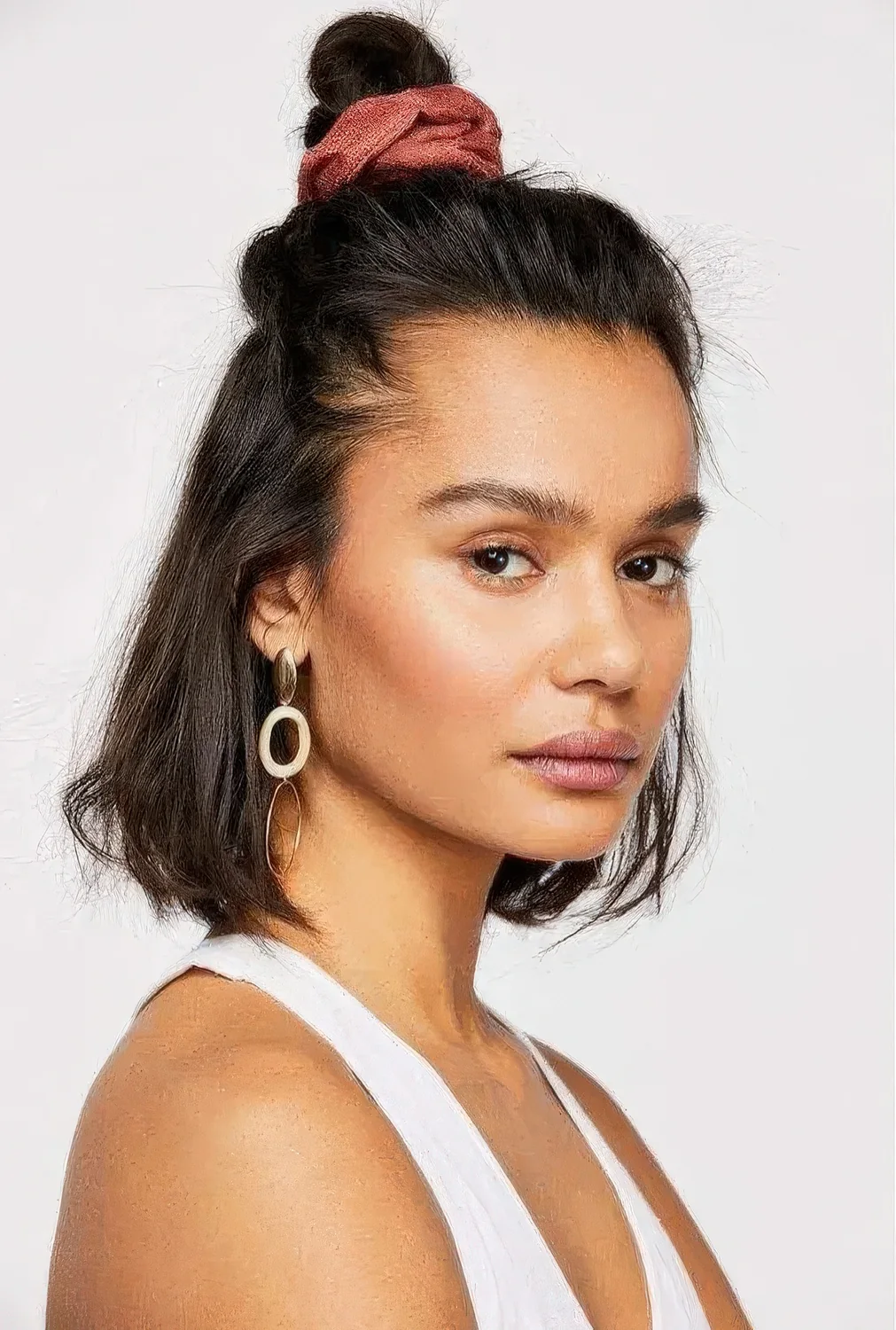 Simple half updo with a top knot and wavy hair down, a volume on top and a red scrunchie to secure the knot.