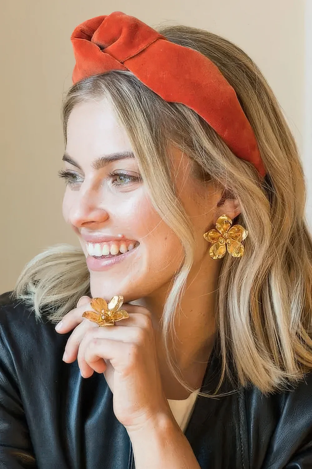 Wavy hair down accented with an orange velvet headband for a bold and refined loo, and floral jewelry.