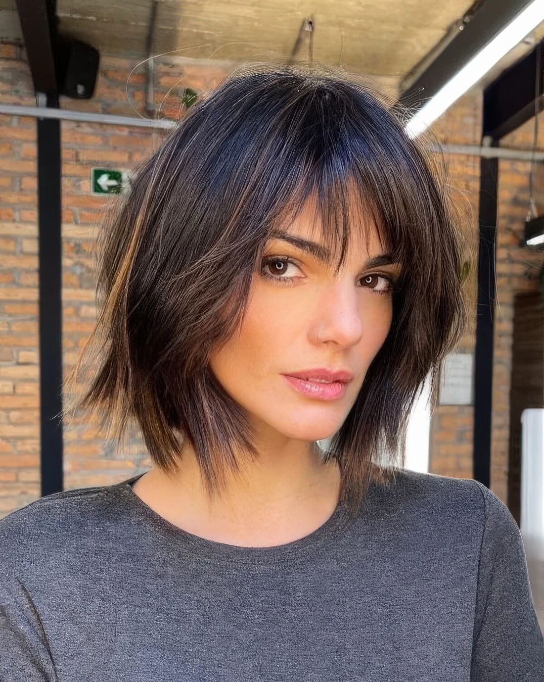 Dark brown shaggy long bob with caramel highlights and bottleneck and wispy bangs.