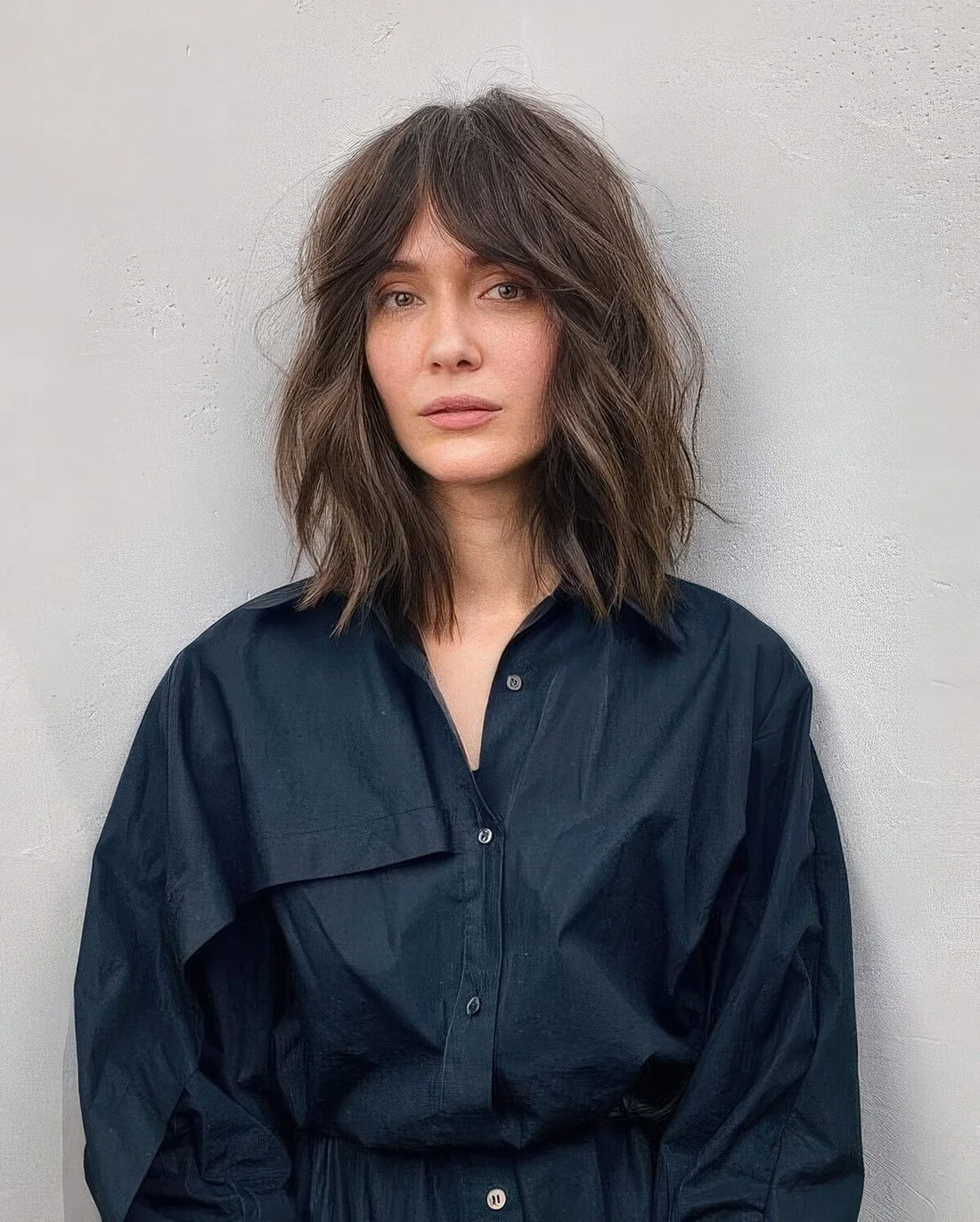 Long brown bob with slight highlights, messy waves and bottleneck bangs.