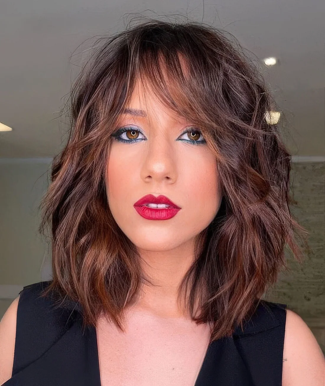 Rich brown long bob with caramel balayage and messy waves plus bottleneck bangs.