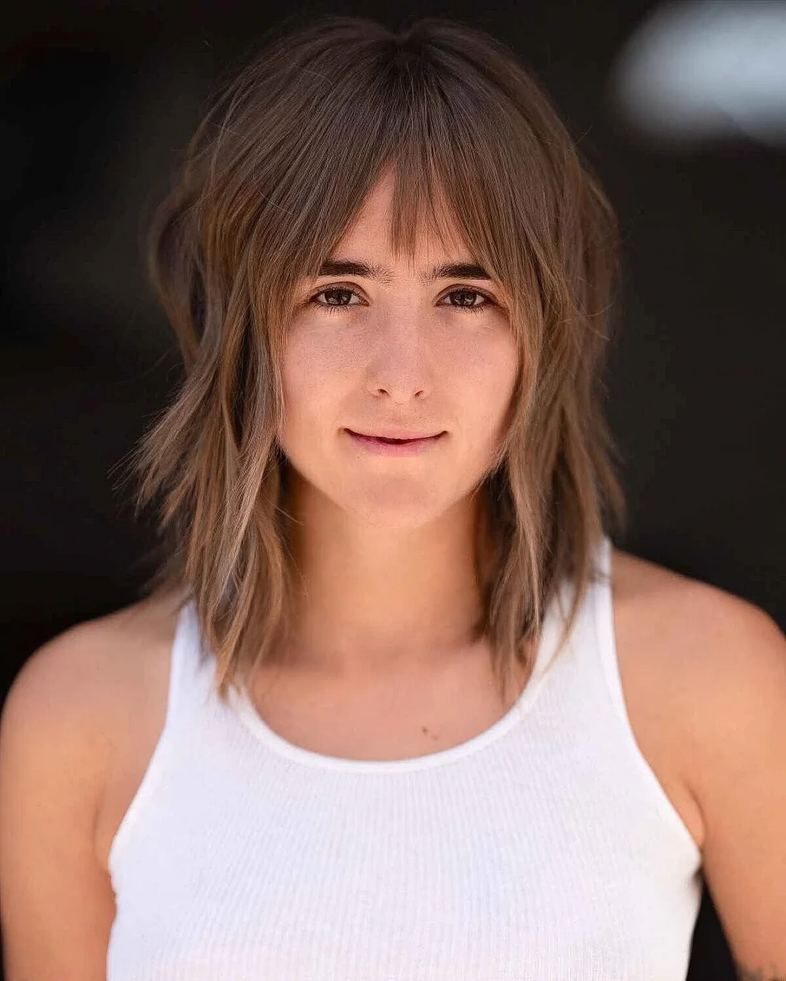 Layered brown bob with caramel highlights and curtain plus wispy bangs.