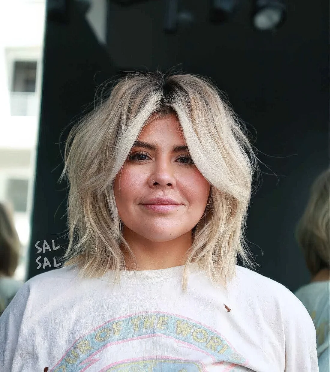 Messy blonde long bob with a darker root and textured waves plus curtain bangs.