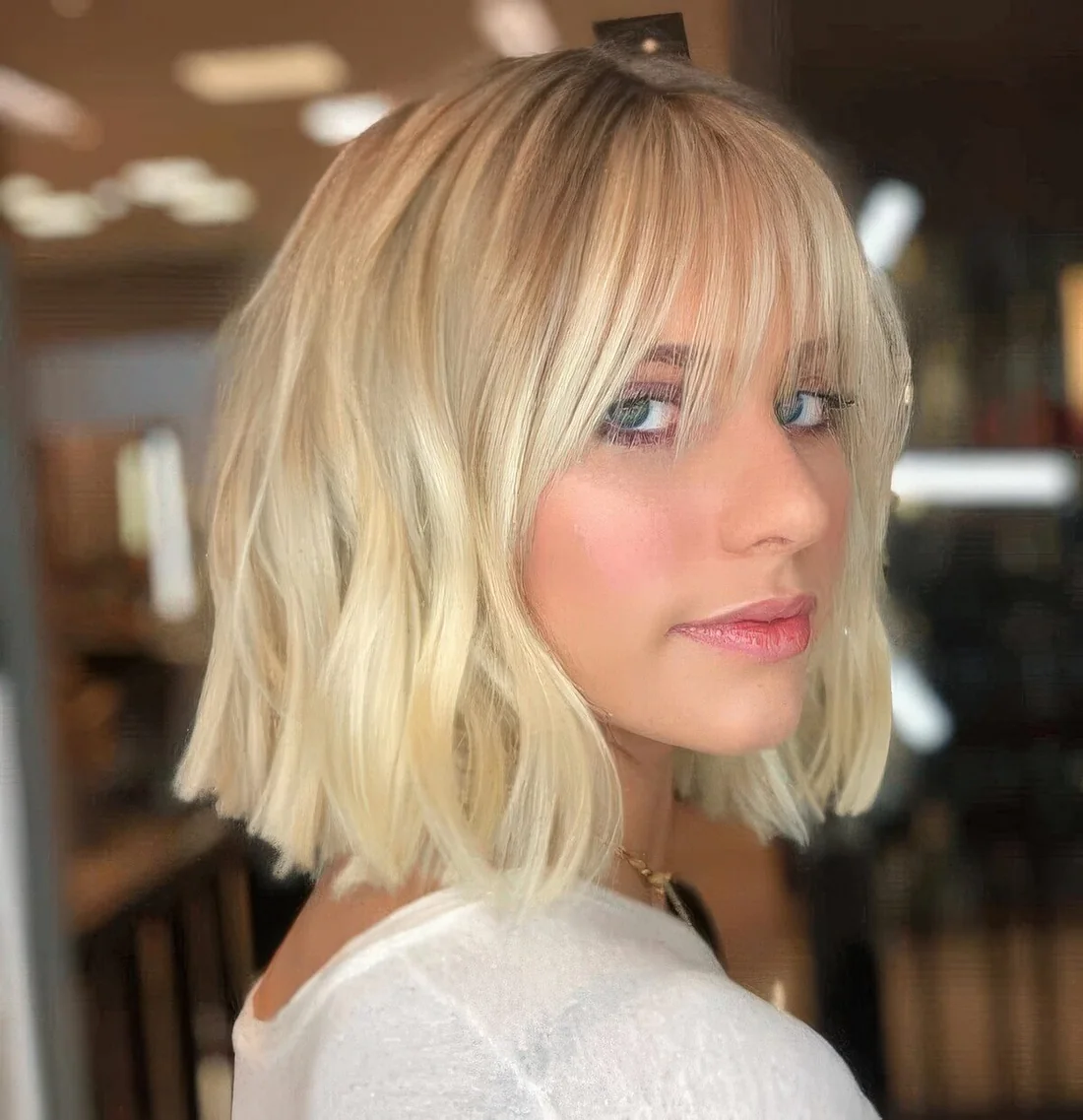 Long blonde bob with waves and wispy bangs.