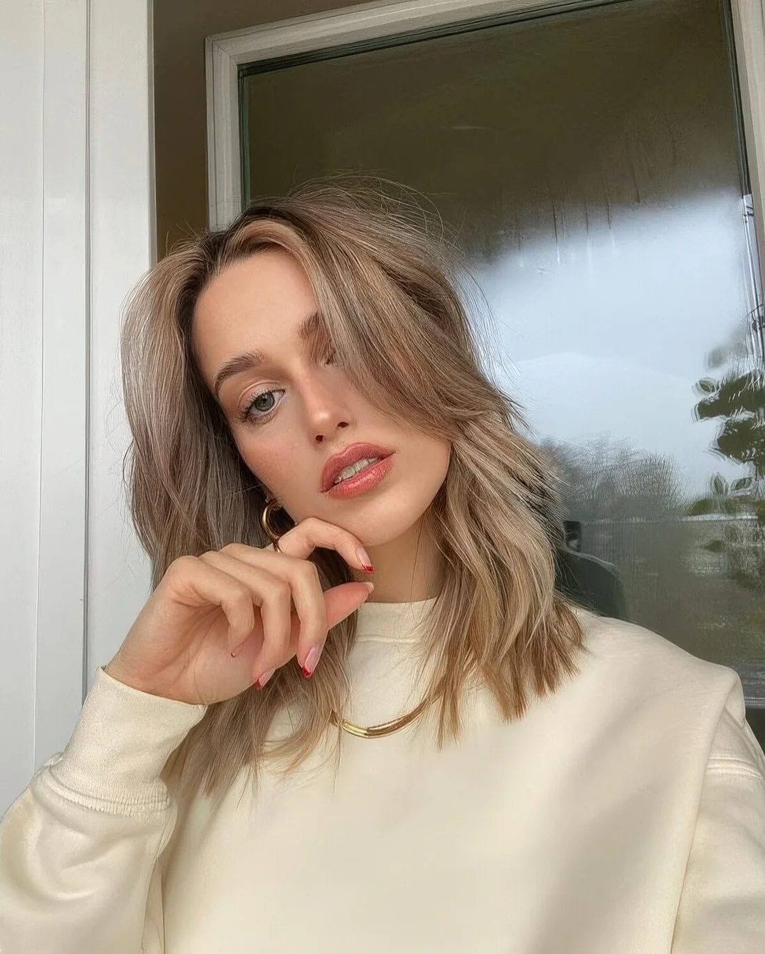 Mushroom blonde shade, medium wavy hair and long curtain bangs for a stylish and relaxed look.