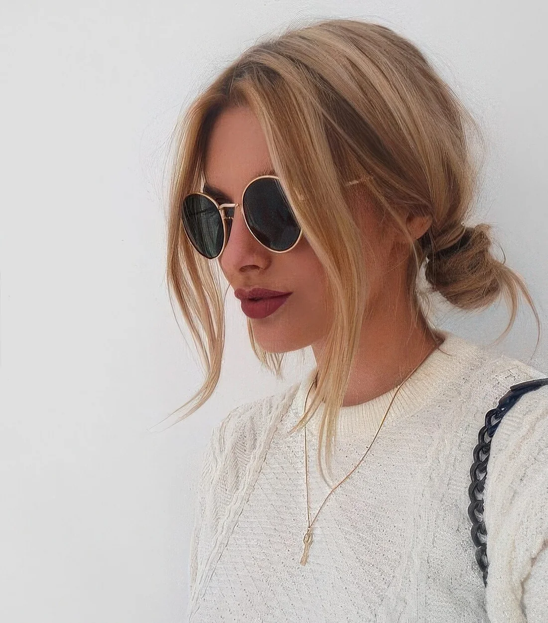 Blonde balayage hair in a low messy bun plus long curtain bangs that beautifully frame the face.