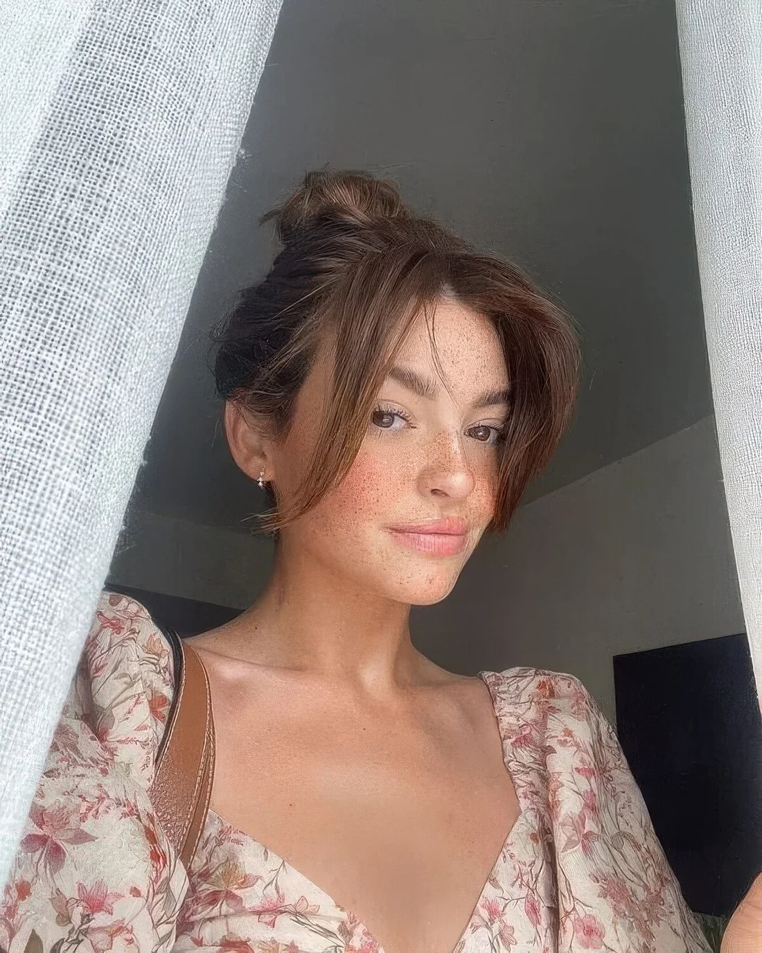 Dark brown hair styled in a top knot and long curtain bangs are a great combo that.