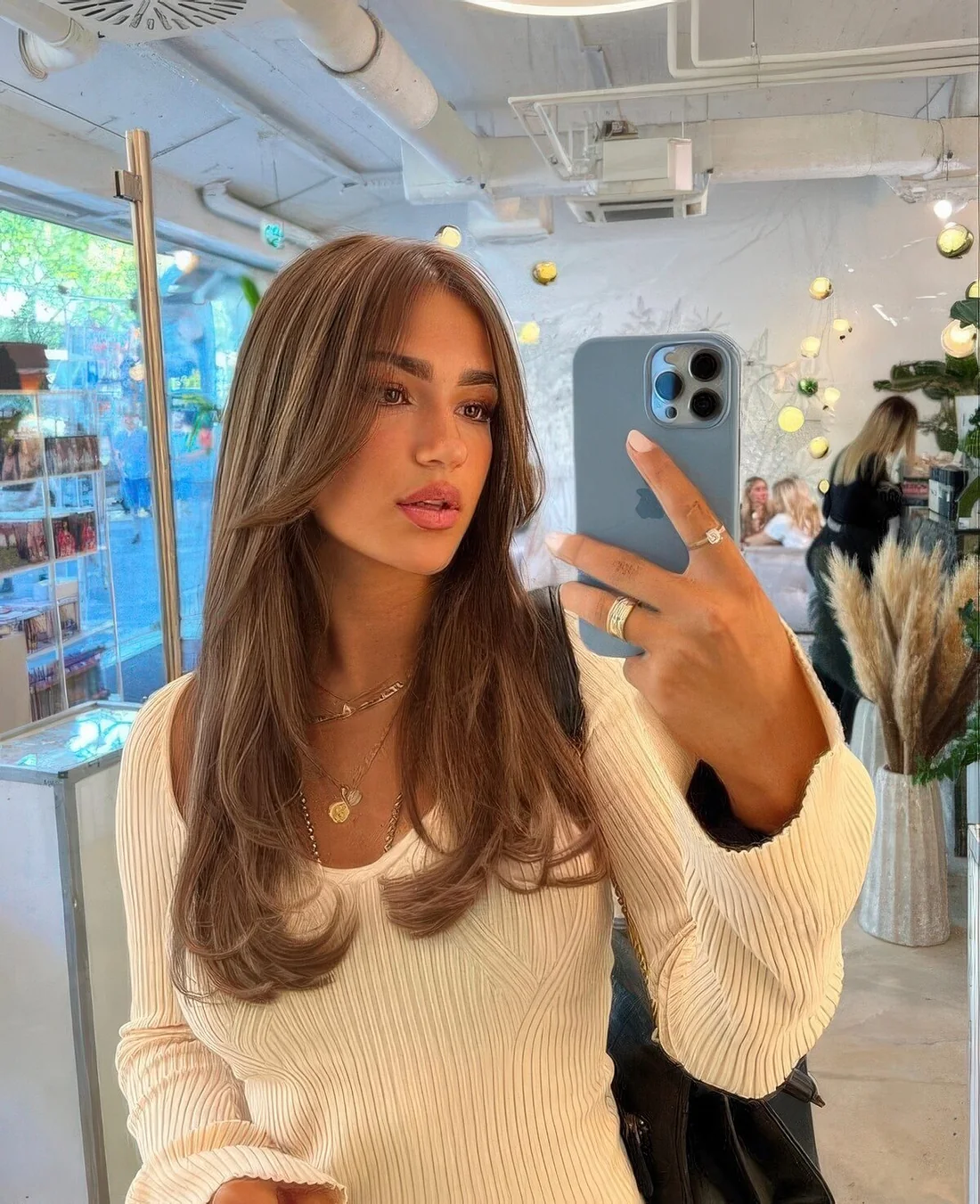 Long brown hair with a cascade effect, a caramel balayage and long curtain bangs.