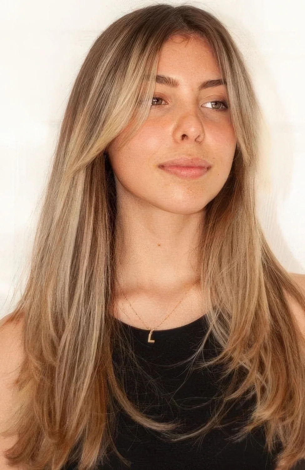 Long light brown hair with caramel balayage and long curtain bangs adding interest to the look.