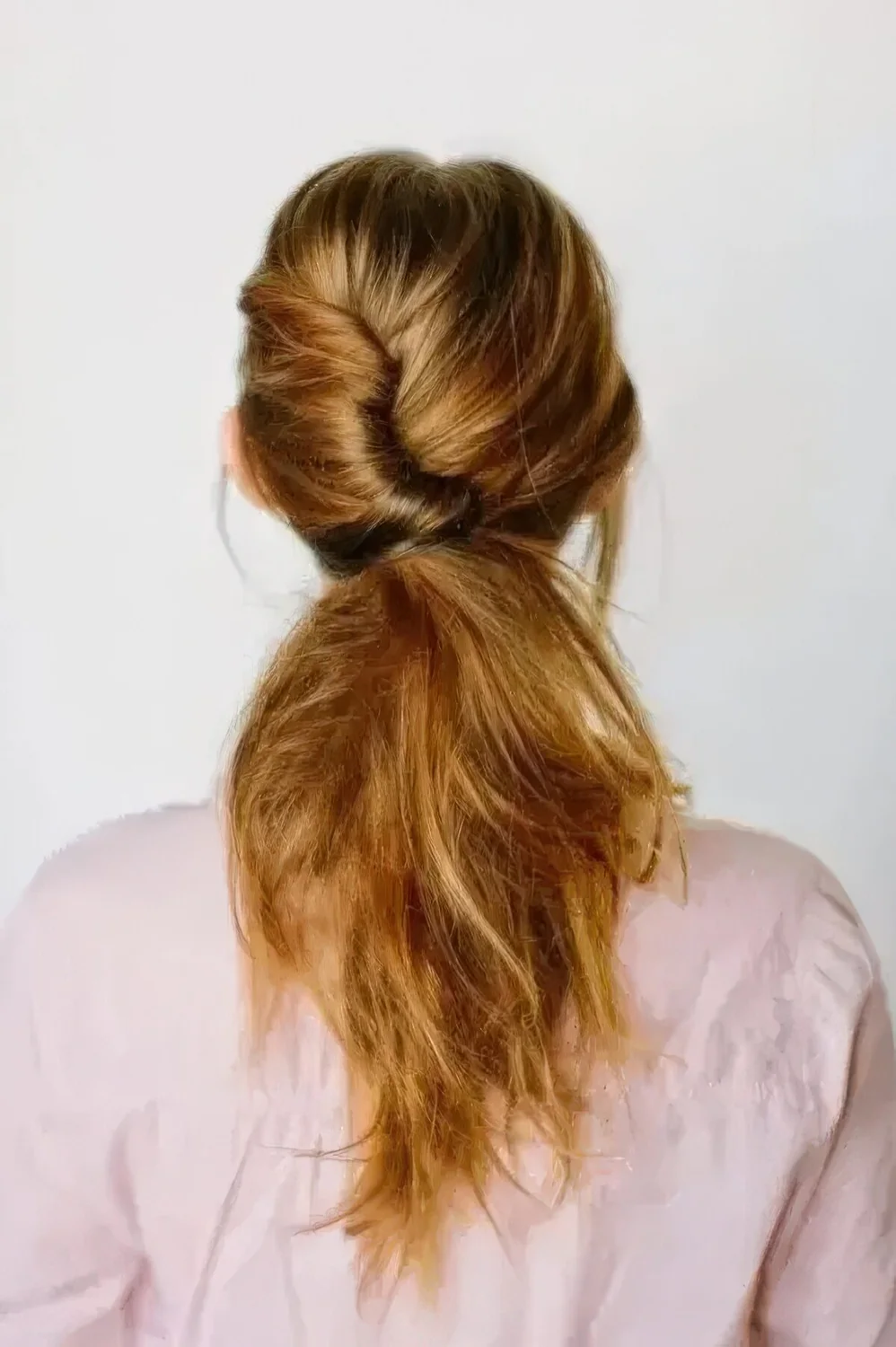 Twisted and textural low messy ponytail with a volume on top and some locks framing the face for a casual bridal or bridesmaid look.