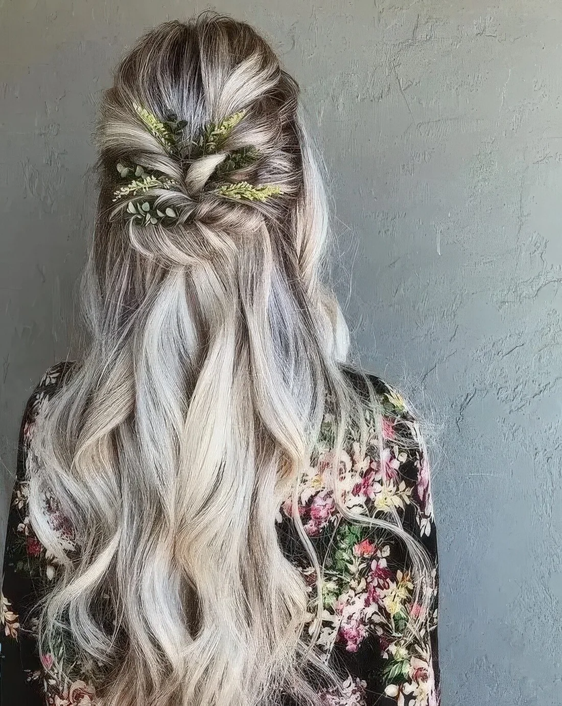 Wavy half updo with a volume on top, twisted greenery decorated element and waves down.