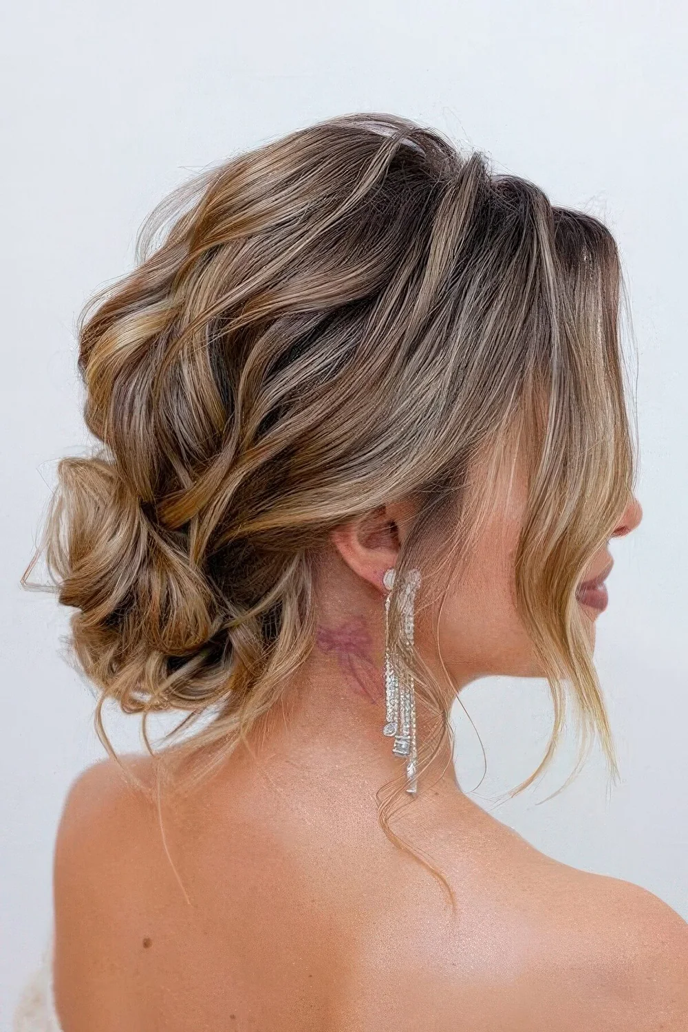 Messy low bun with a wavy top and a wavy bun, some locks framing the face.