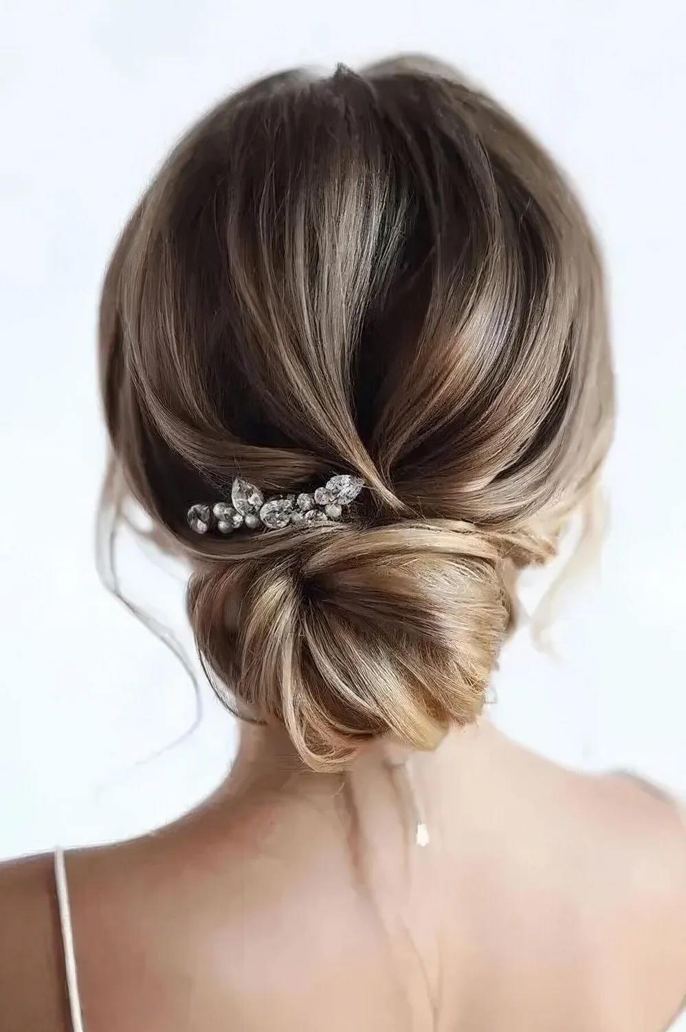 Dimensional low bun with a volumious top and a loose bun plus a rhinestone hairpin.