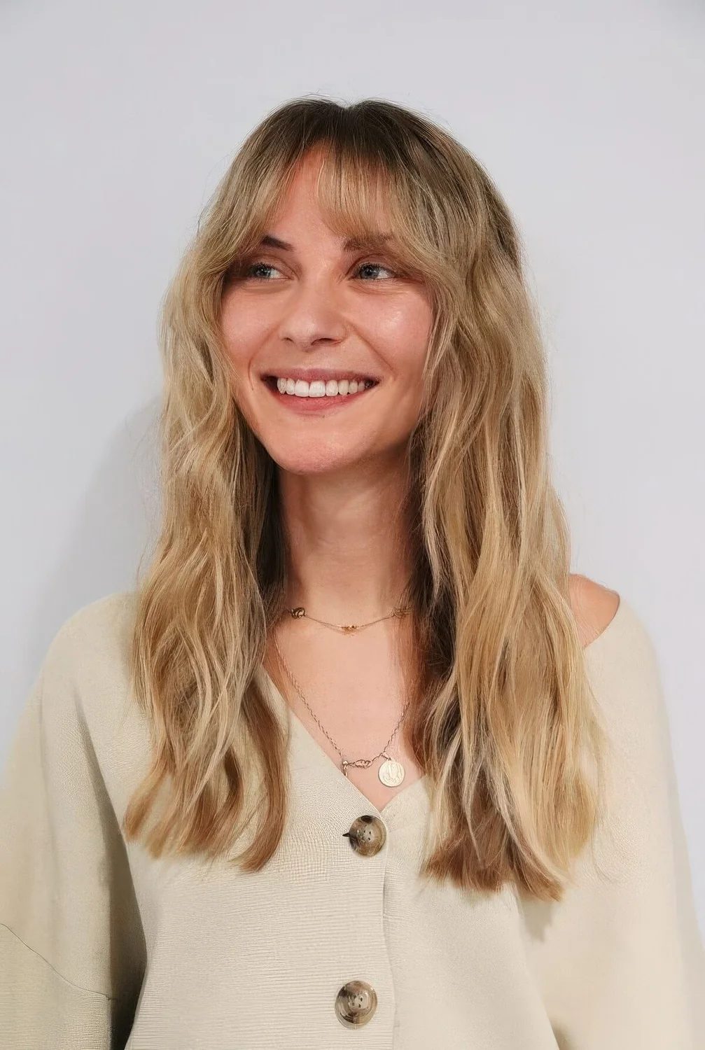 Long blonde hair with dark root and bottleneck bangs.