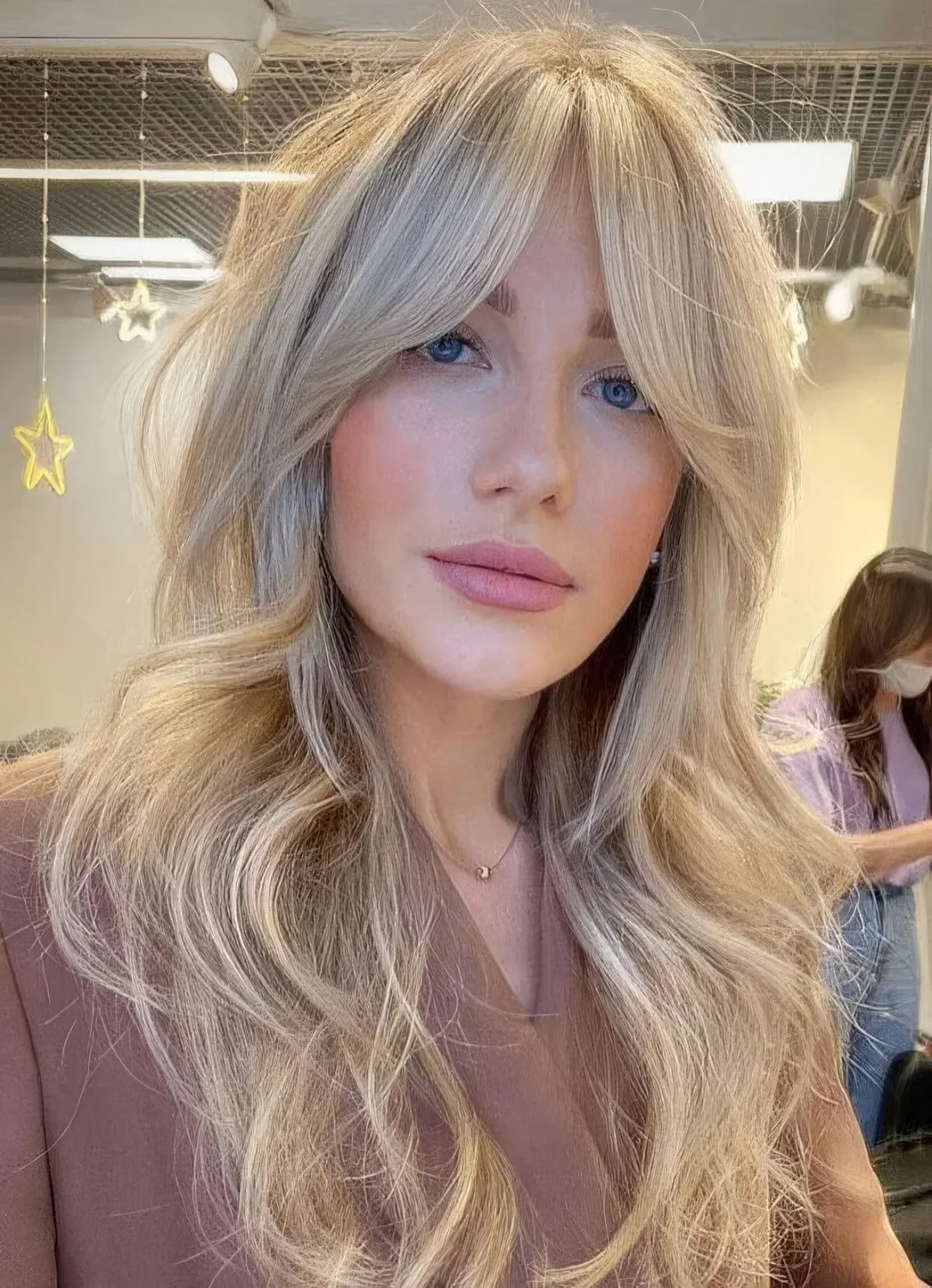 Long creamy blonde wavy hairstyle with curtain bangs.