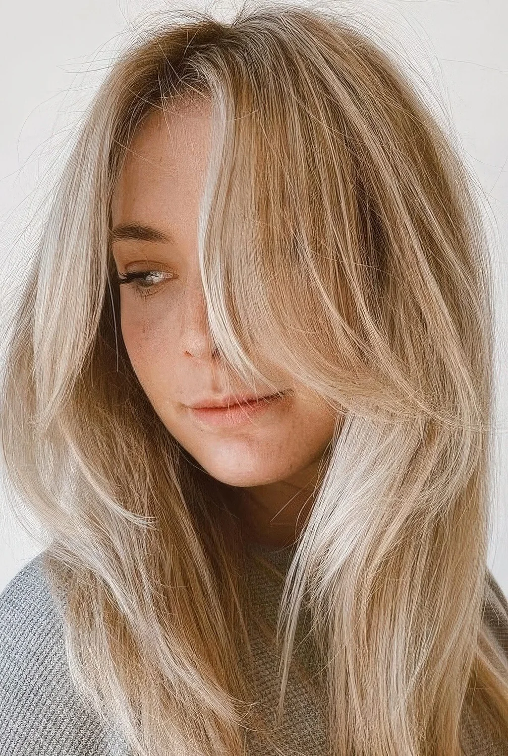 Long blonde hair with icy balayage and chin-length side bangs.