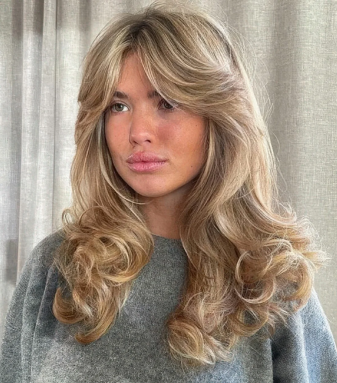 Long blonde hair with layers to remove weight, curls at the ends and soft curtain bangs.