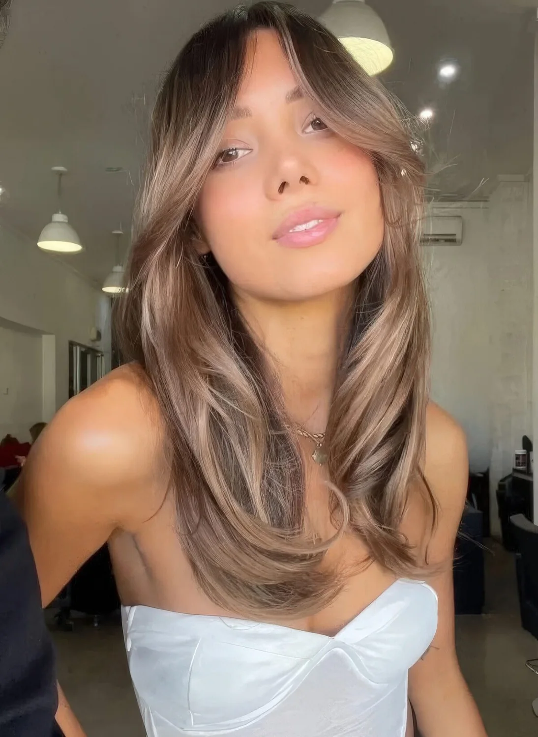 Long light brown hair with lighter accents, chin bangs and curved ends.