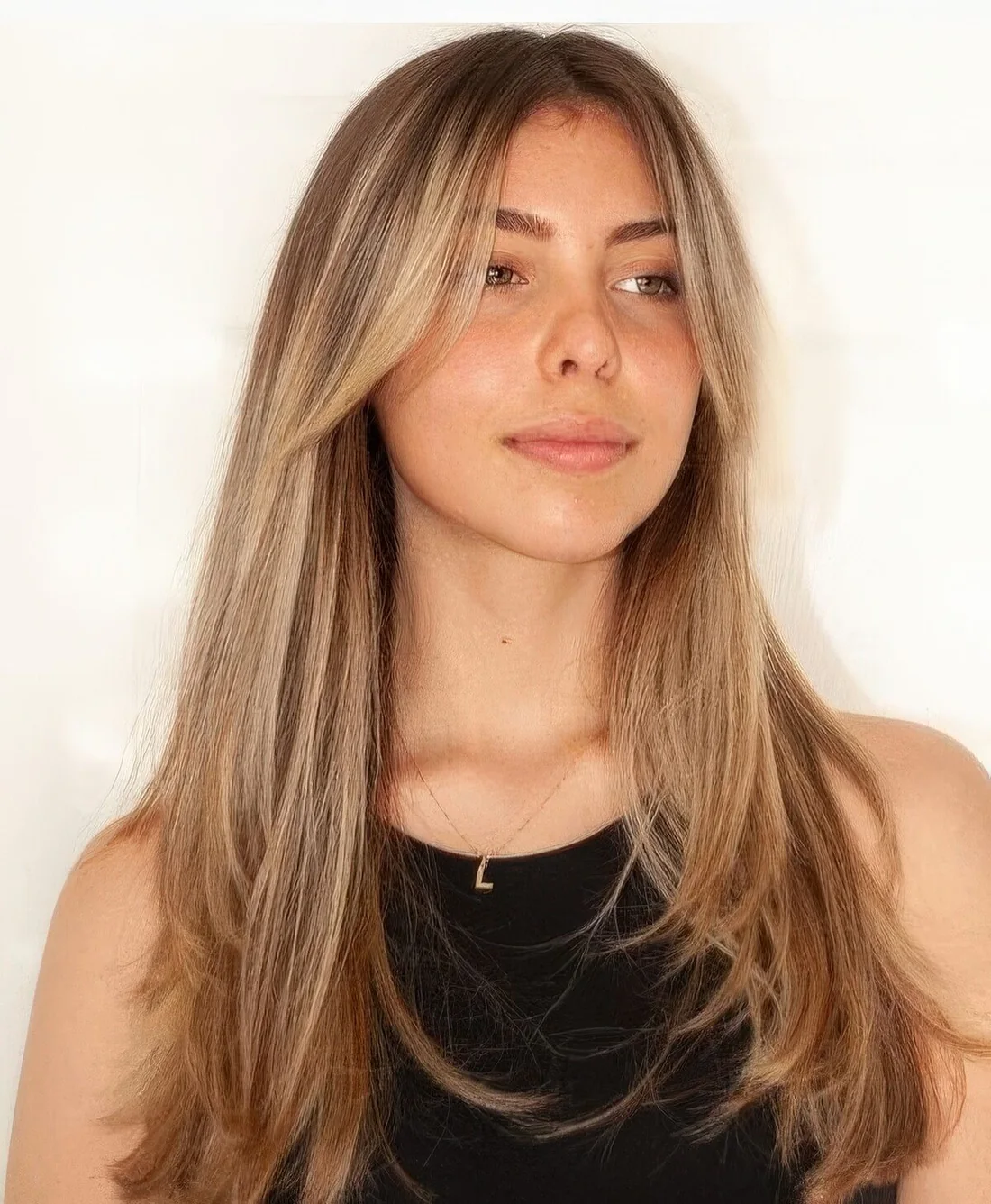 Long hair with warm blonde balayage and with curtain bangs, with much texture.