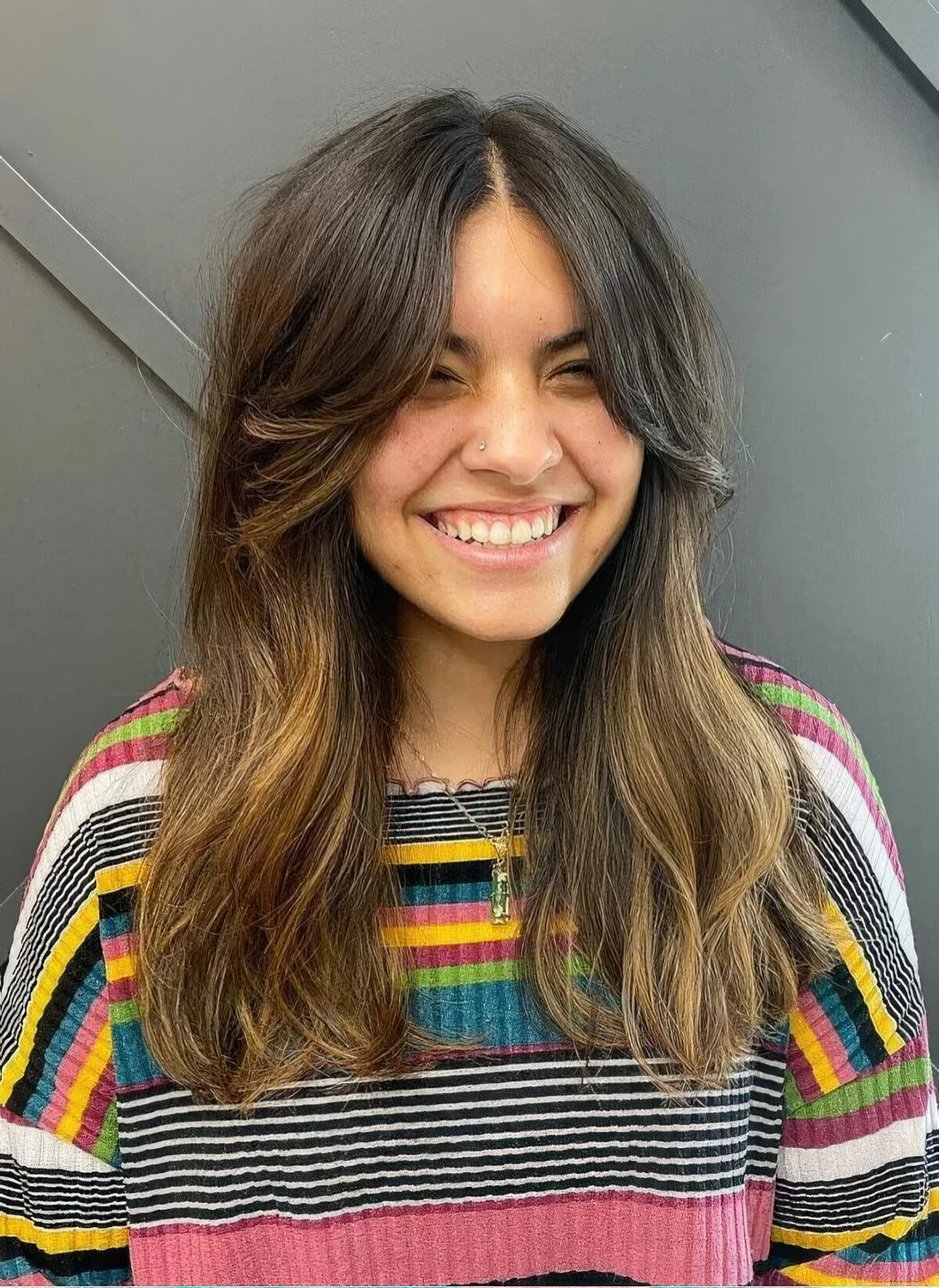 Long dark brown hair with a melted balayage and soft layered curtain bangs.
