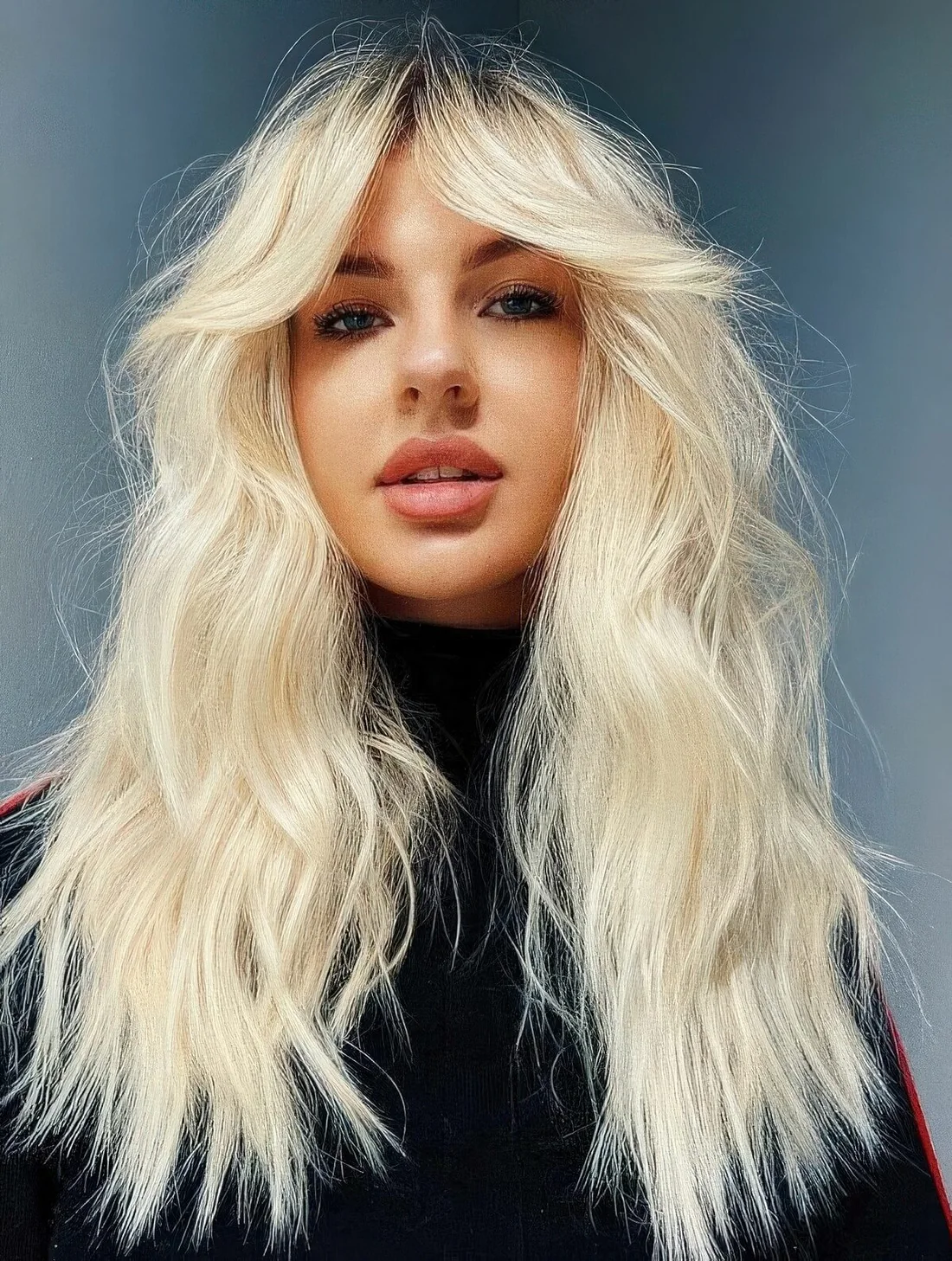 Long textural blonde hair with choppy ends and soft face-framing curtain bangs.