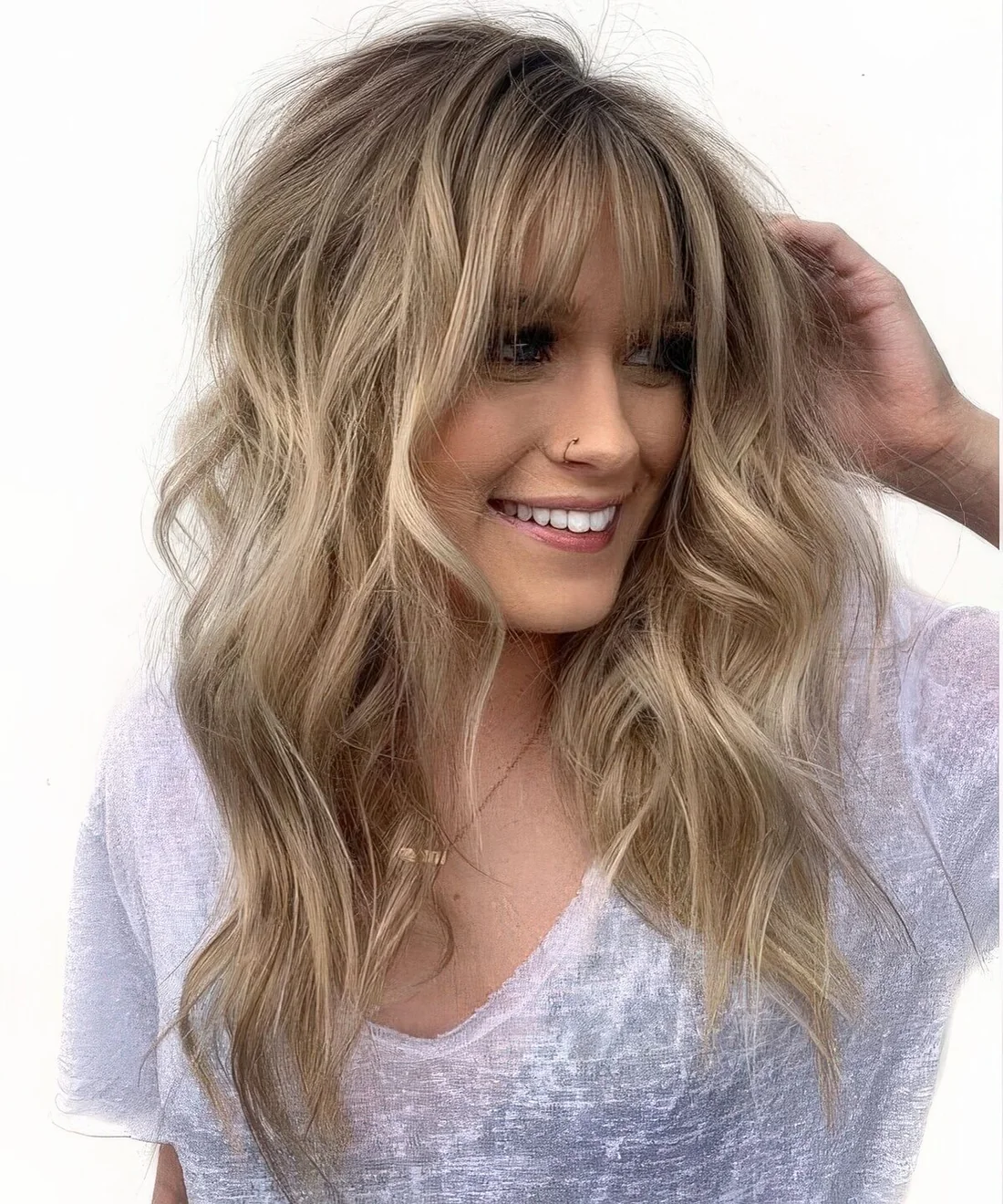 Long wavy londe hair with texture and with balayage plus wispy bangs for a chic touch.