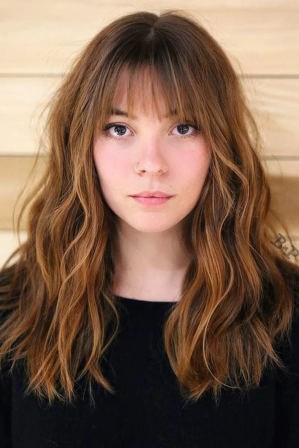 Long cinnamon colored hair with caramel and golden blonde balayage, waves and wispy bangs.