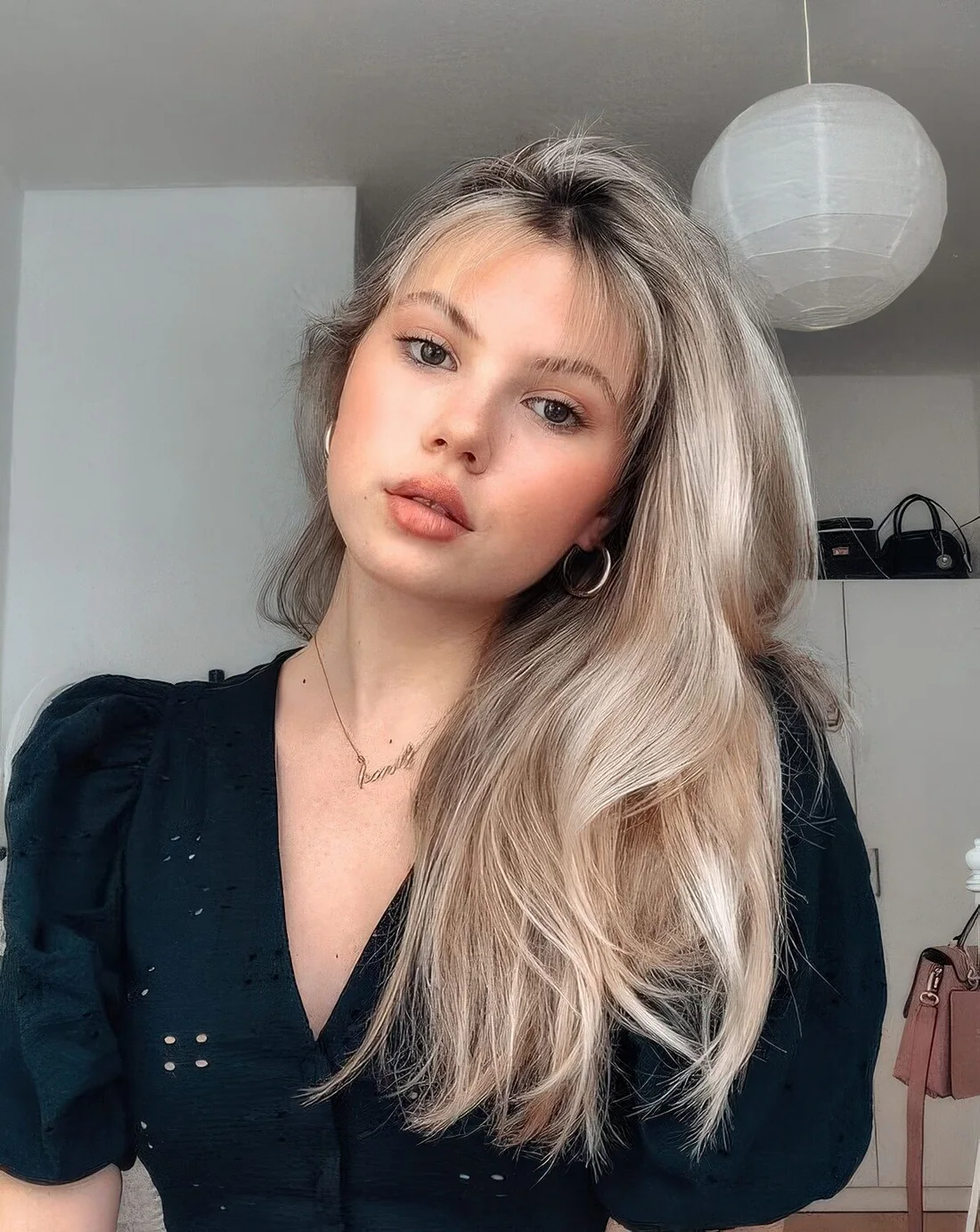 Long icy blonde hair with balayage of a warmer tone, a dark root and wispy bangs for a delicat elook.