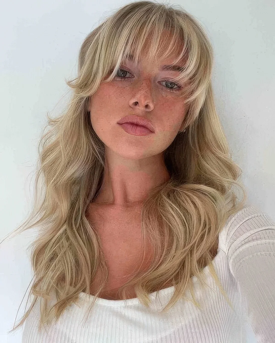 Long blonde hair with layers and waves plus wispy and curtain bangs paired to frame the face in the most beautiful way.