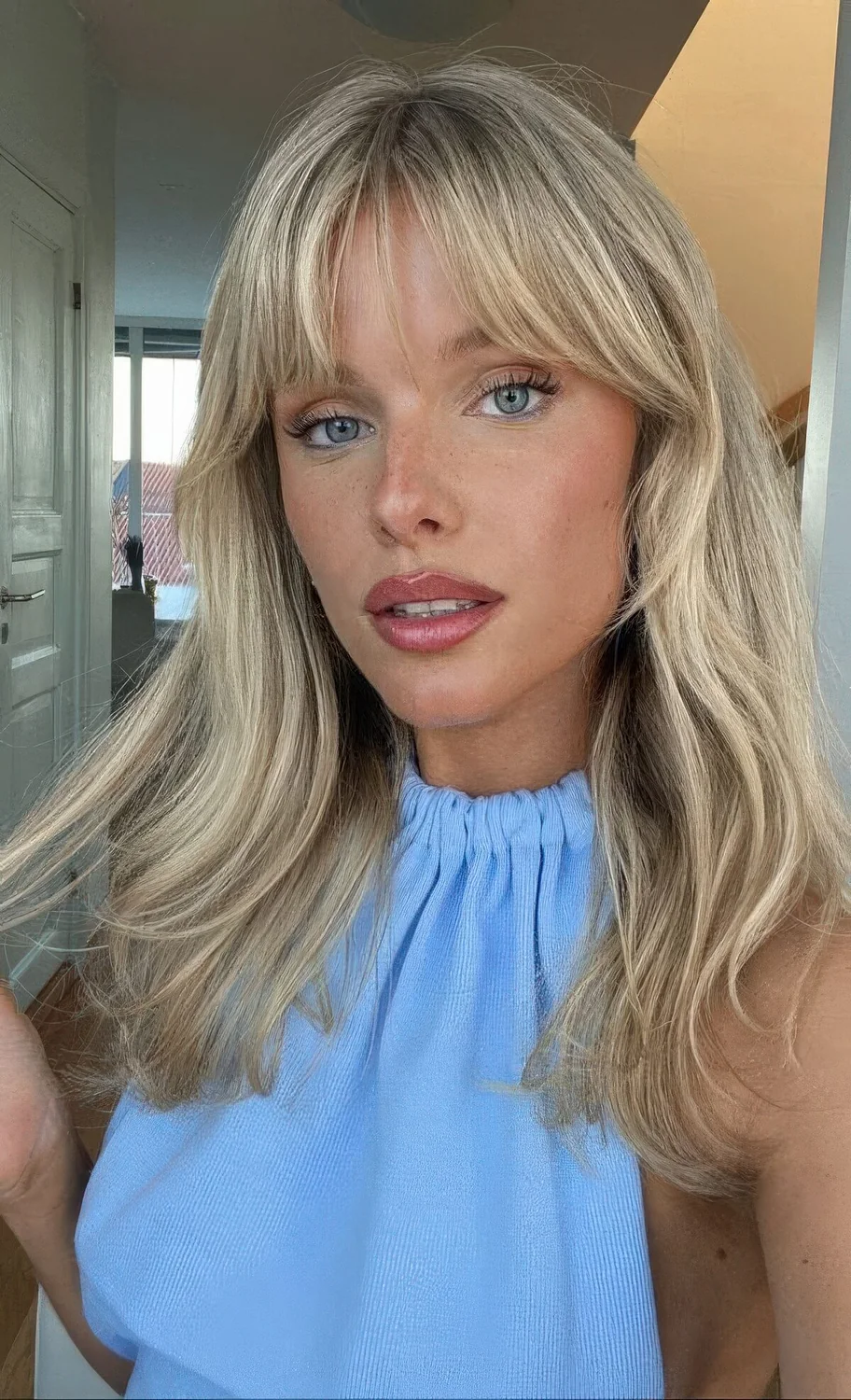Long blonde hair with waves and layered bangs, with curtain and wispy ones.