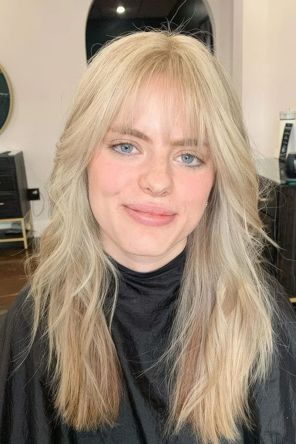Long blonde hair with waves and wispy bangs.
