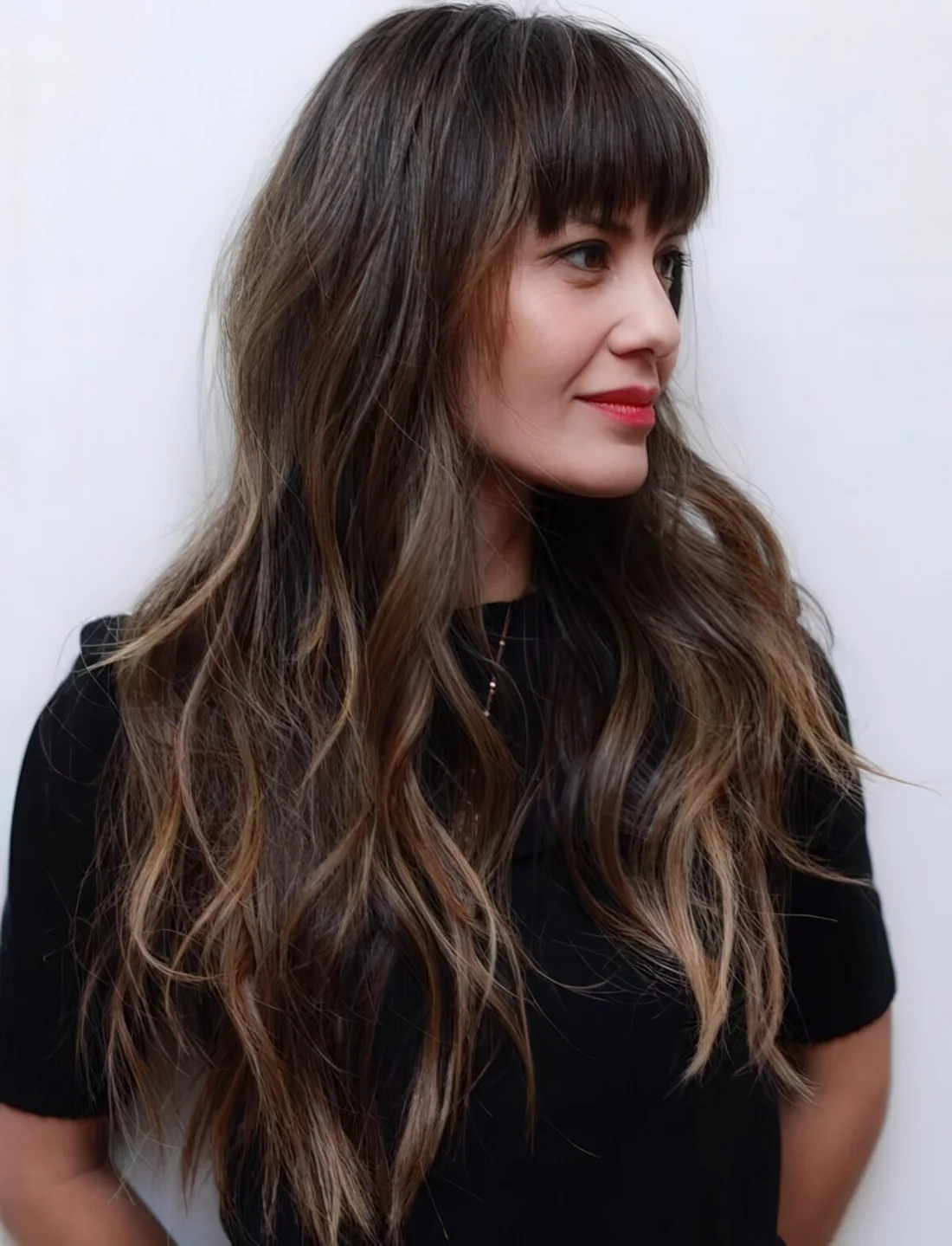 Long layered haircut with balayage and eyebrow skimming bangs for an effortless look.