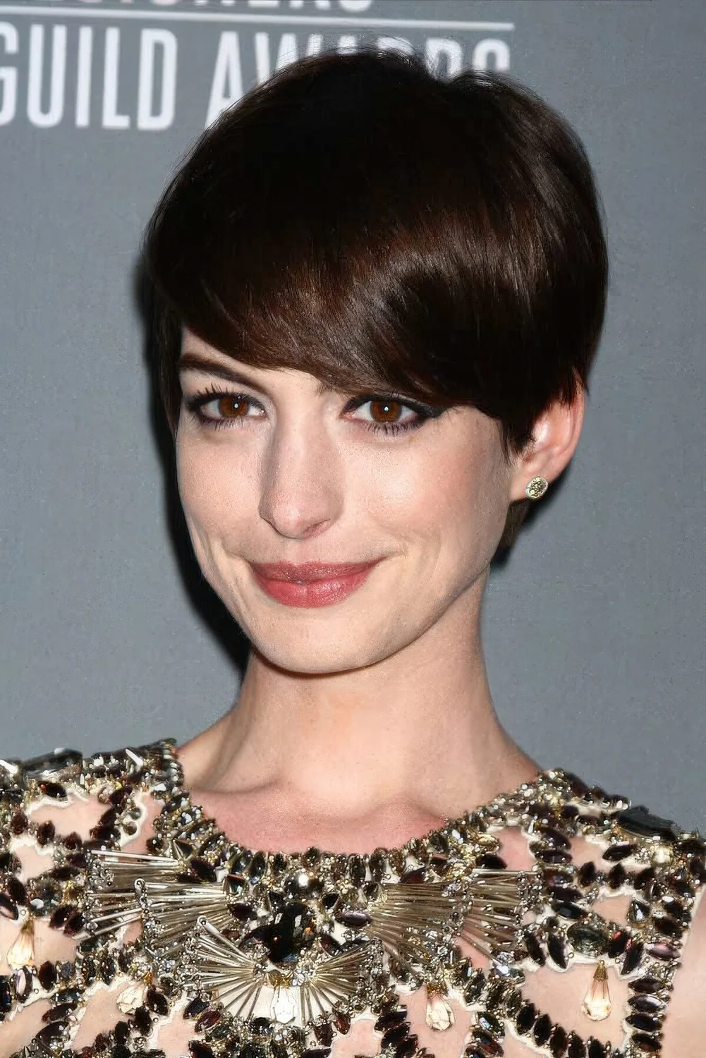 Anna Hathaway wearing a long dark brown pixie that emphasizes the beauty of the face farming it.