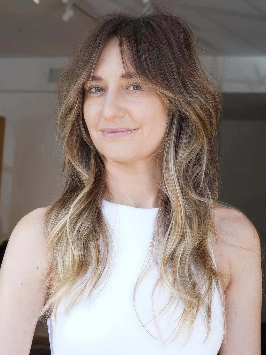 Brunette wolf cut with bottleneck bangs and waves down plus blonde balayage.