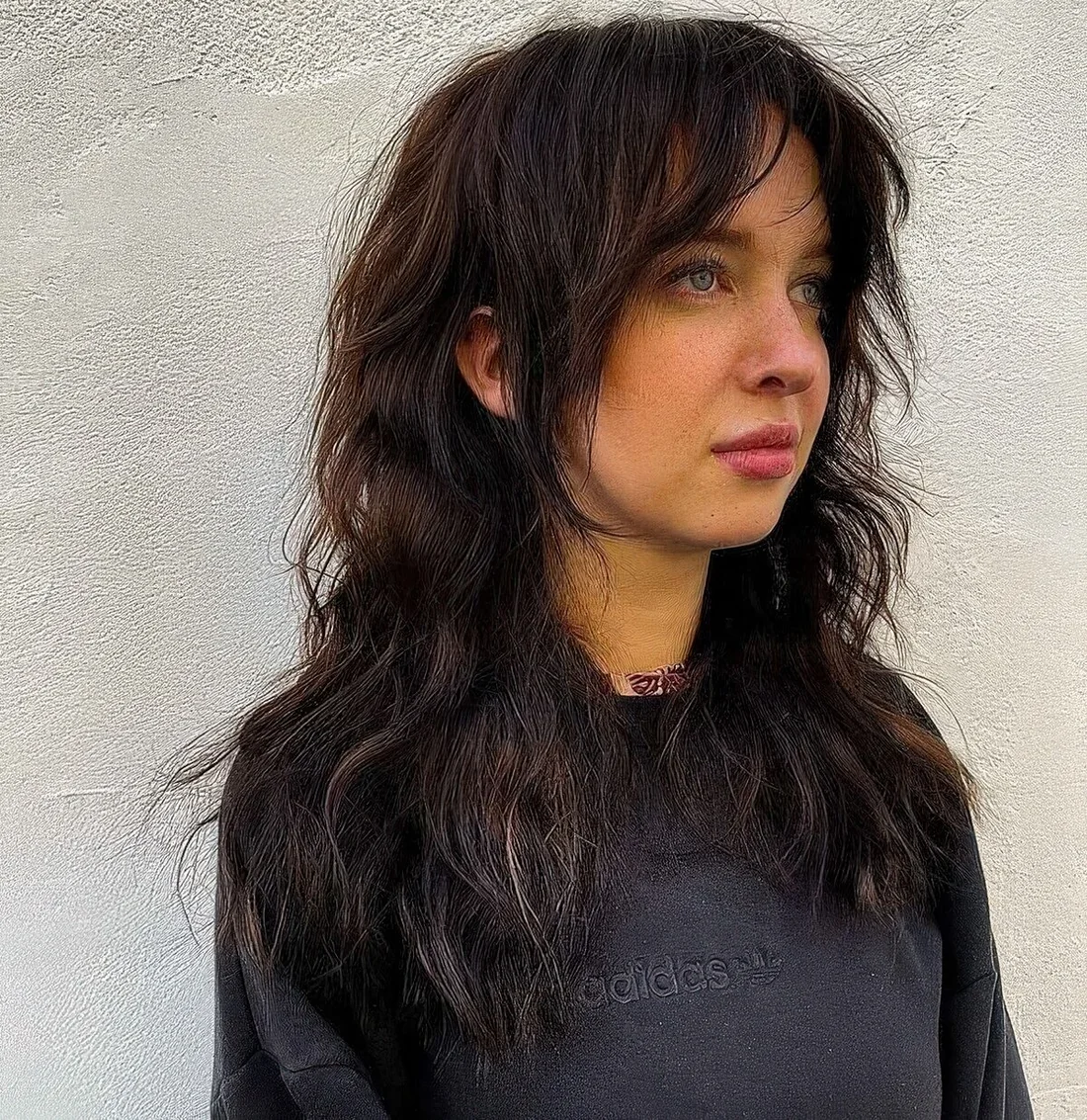 Dark brunette long wolf haircut with curtain bangs and face-framing layers and messy waves.