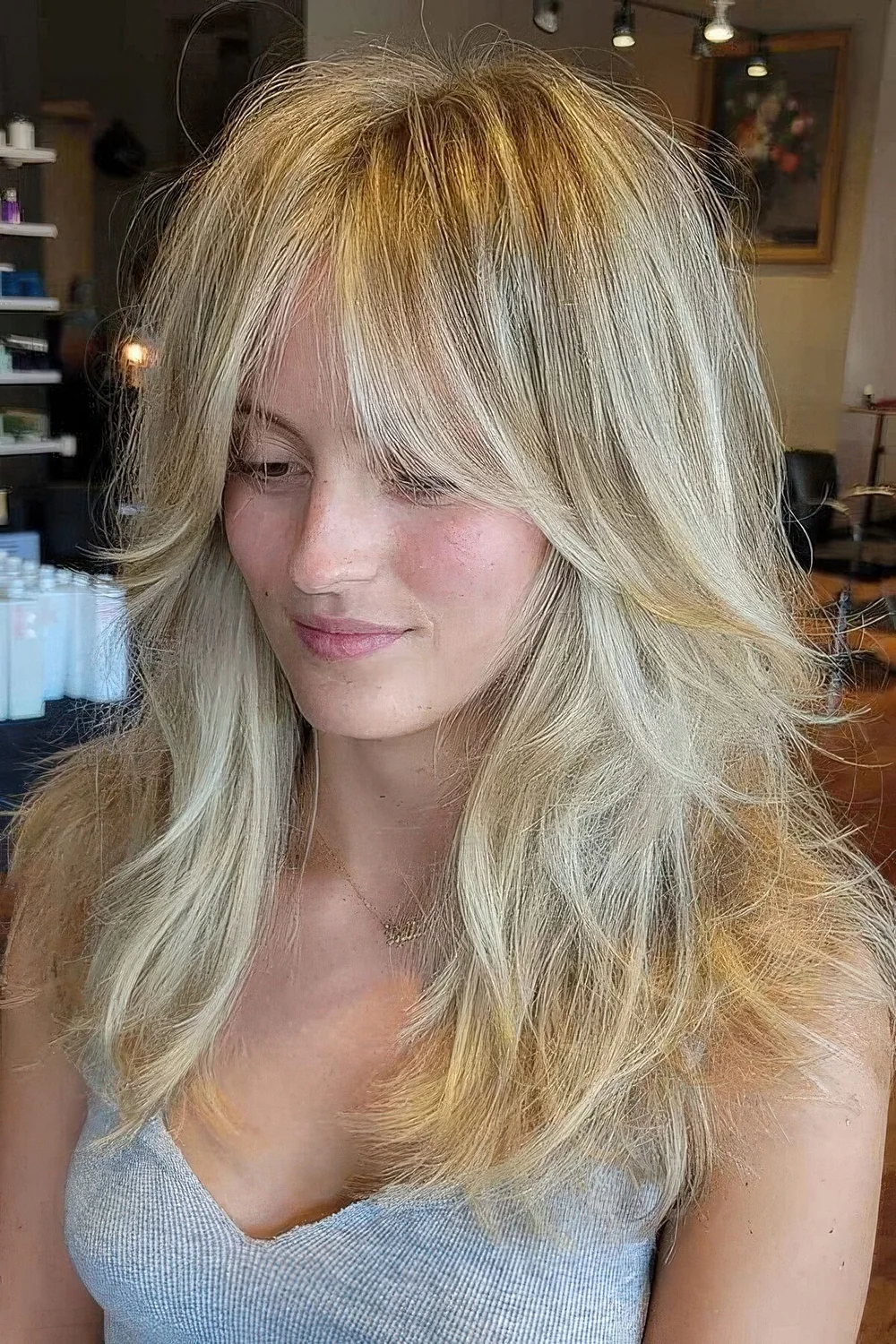 Long blonde wolf haircut with curtain bottleneck bangs, messy waves down.