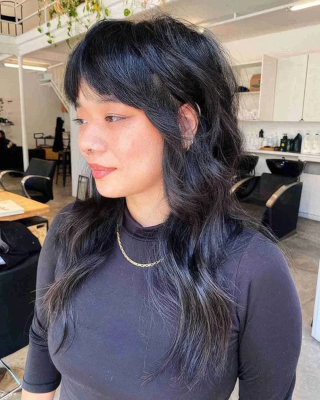 Long black wolf cut with bottleneck bangs and wavy hair with a bit of volume.